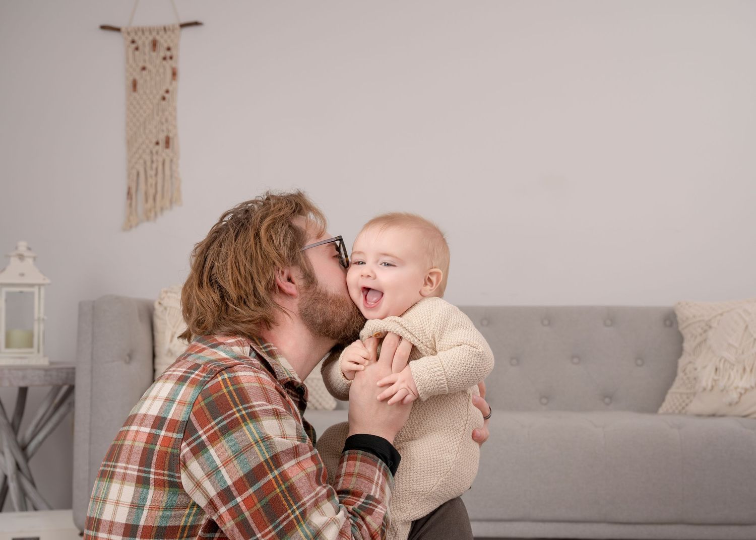 A joyful moment shared between a baby in cream clothing and someone in a plaid shirt in a cozy living room setting. Princeton MN Milestone,