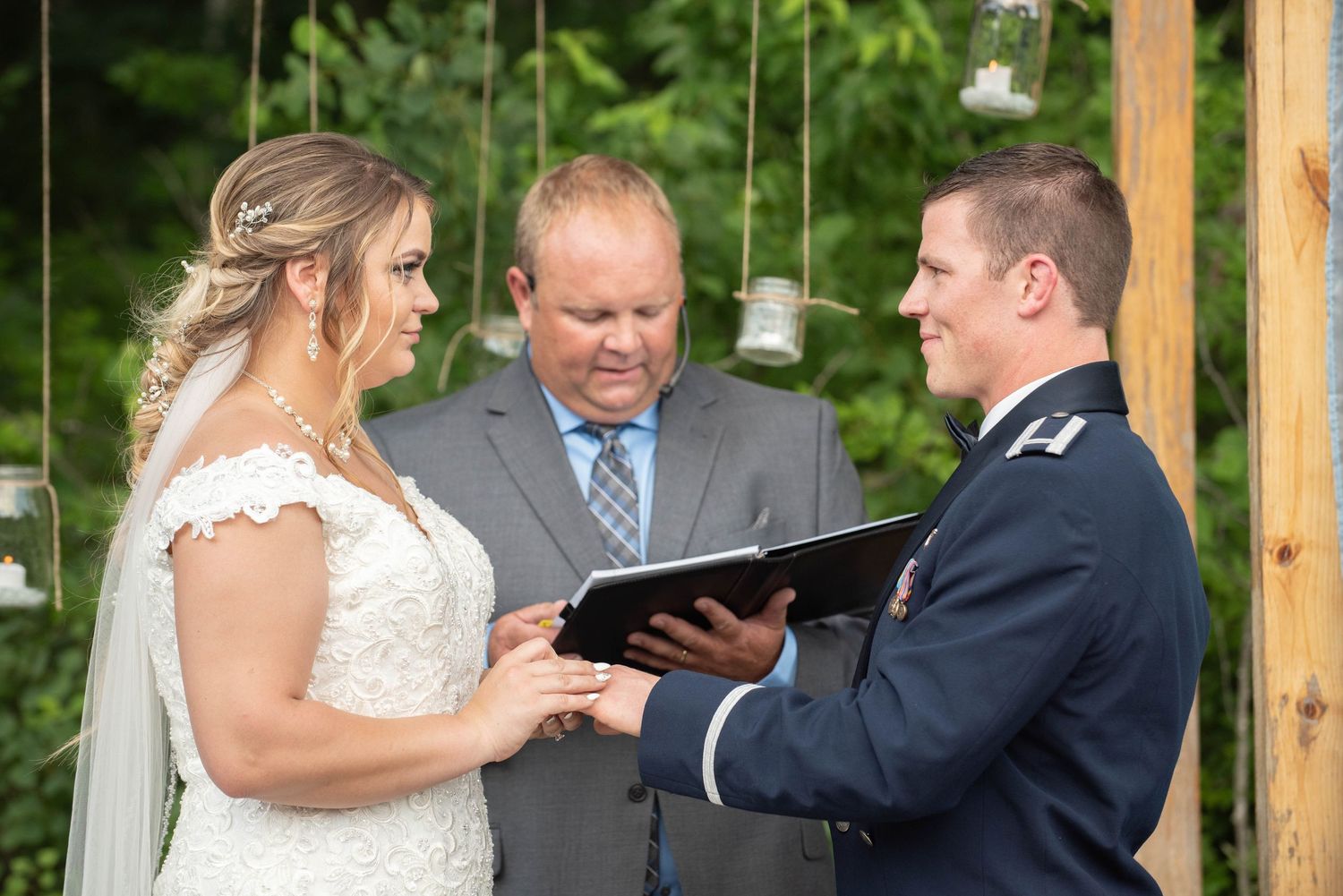 Couple exchanges vows during a garden wedding ceremony under wooden posts with draped fabric. Zimmerman MN Weddings