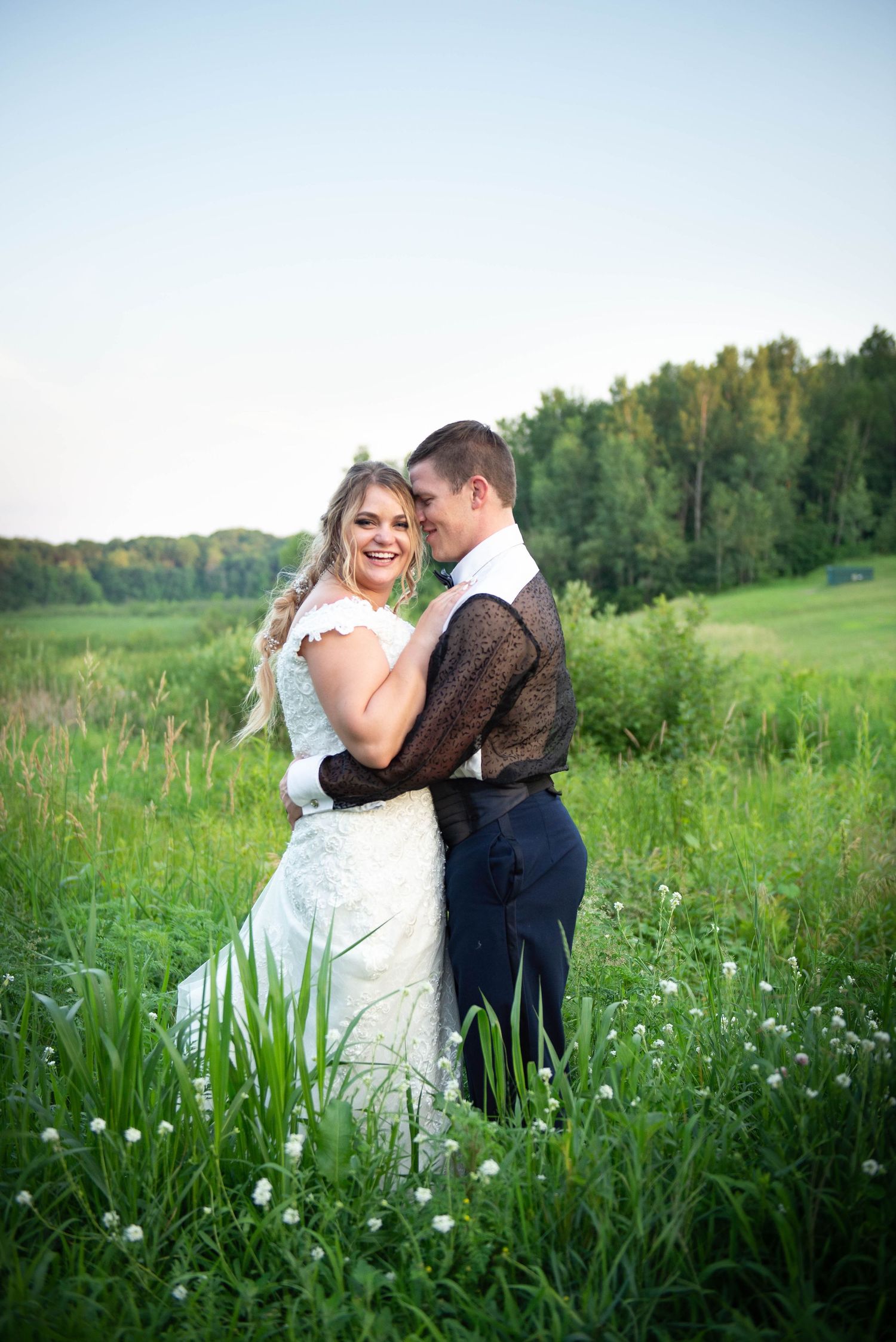 Couple embracing in a summer meadow with wildflowers and golden evening light. Zimmerman MN Weddings