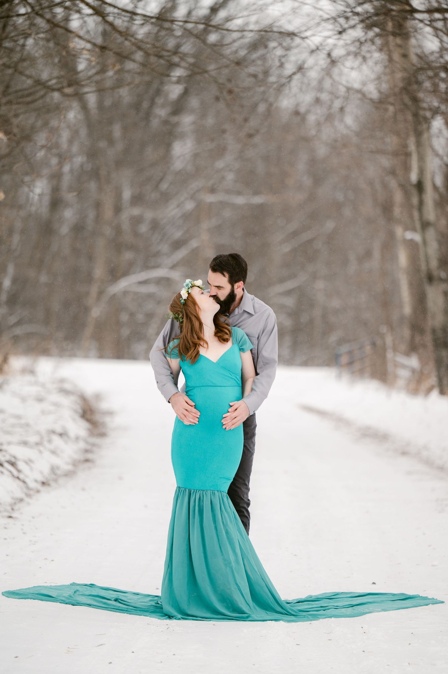 A couple shares an intimate embrace while standing in a snow-covered winter landscape.