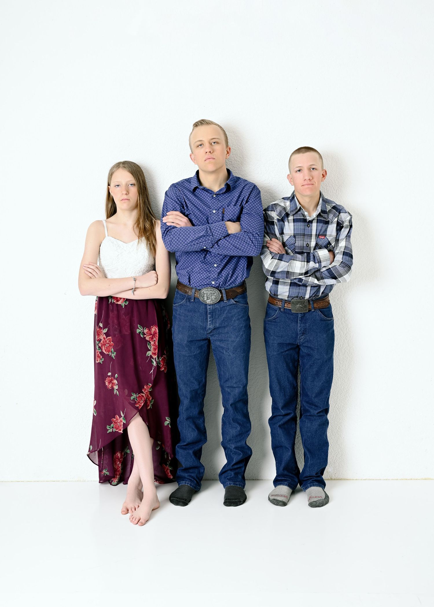 Family portrait against white wall shows three people standing with arms crossed in coordinated casual outfits.