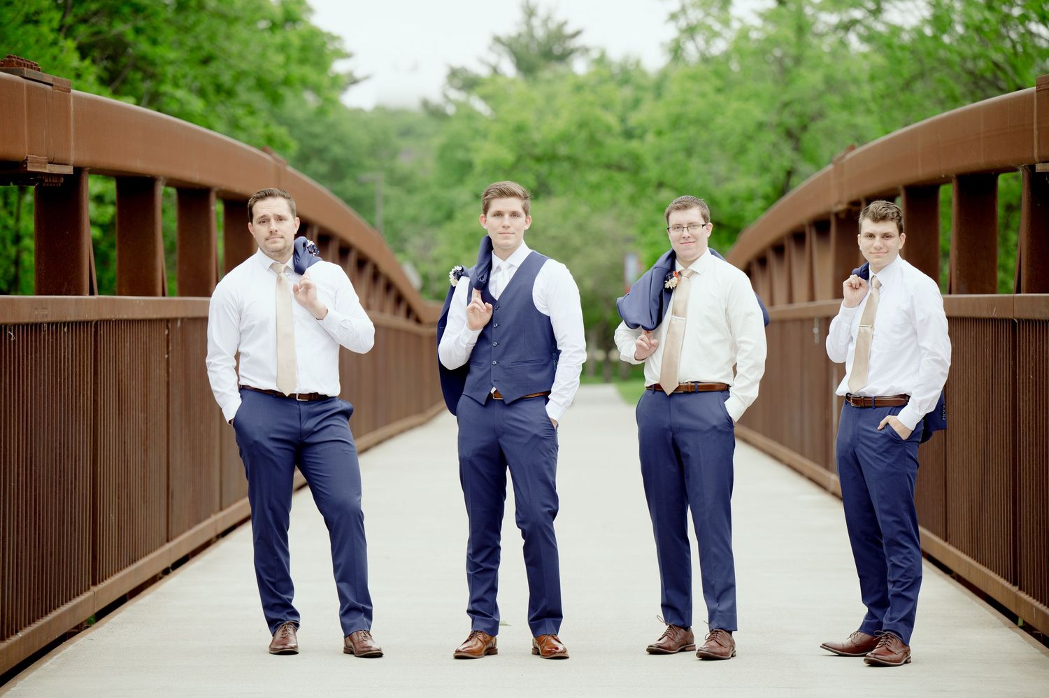 Fun sequence of groomsmen in navy suits doing dance moves on a wooden bridge.