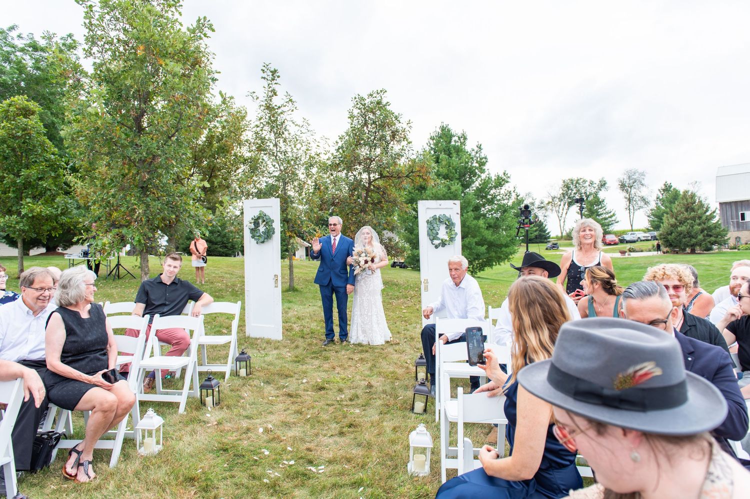 Wedding guests seated in white chairs on a grassy lawn during an outdoor ceremony.