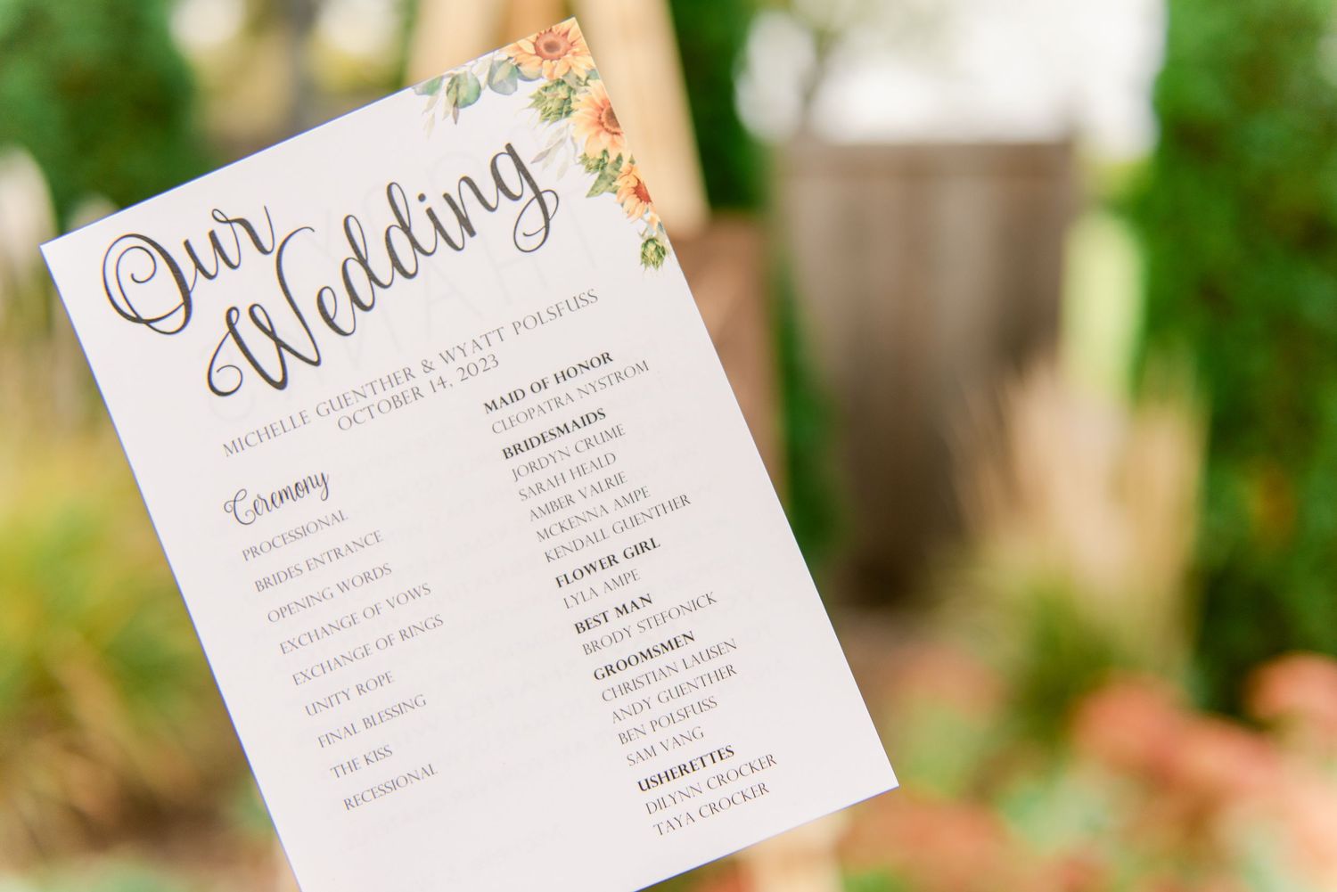 Central MN Wedding Photos - Close-up of a floral wedding program with elegant script displayed at an outdoor autumn ceremony.