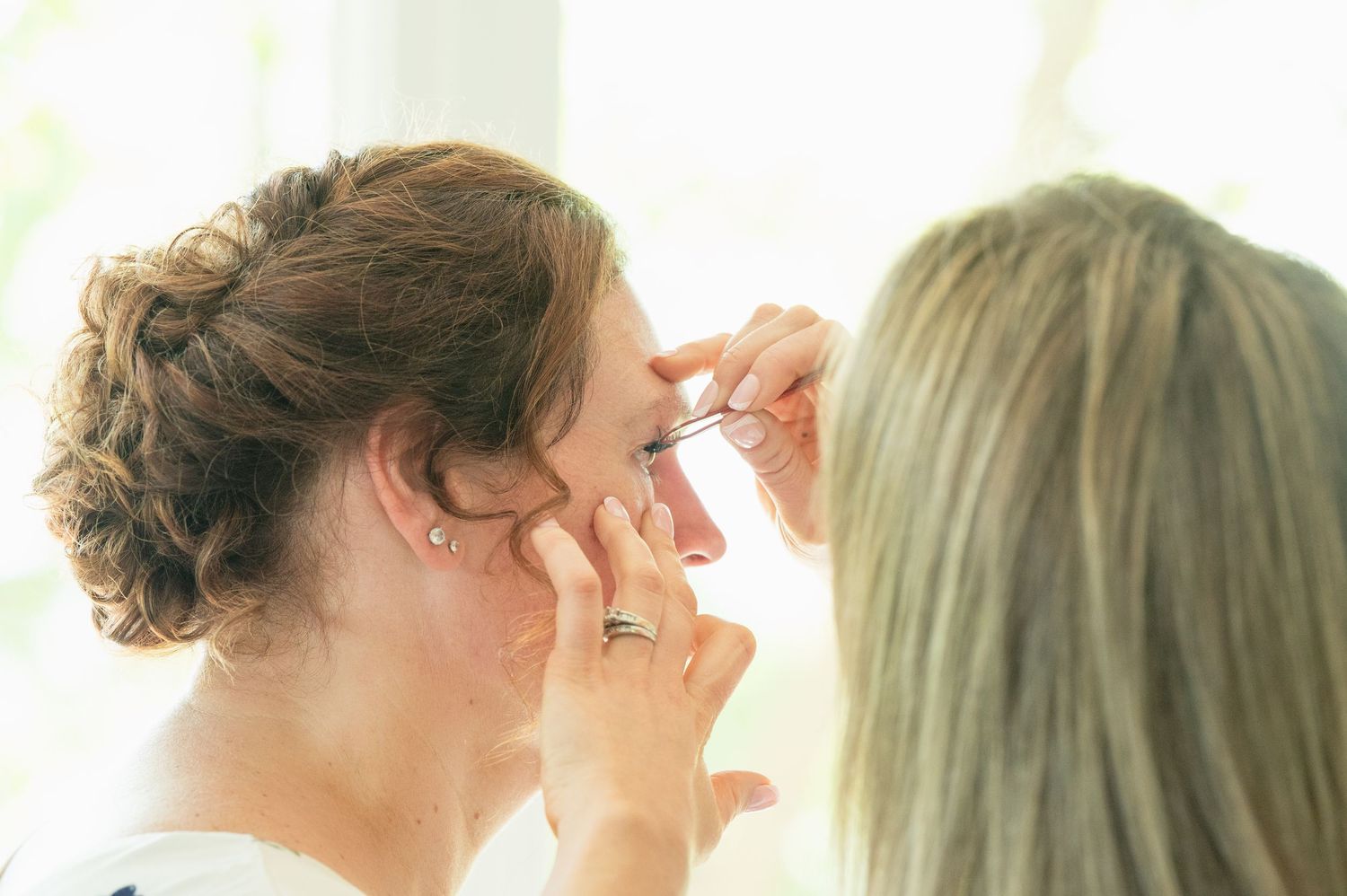 A makeup artist applies false eyelashes to a brunette bride during wedding preparations.