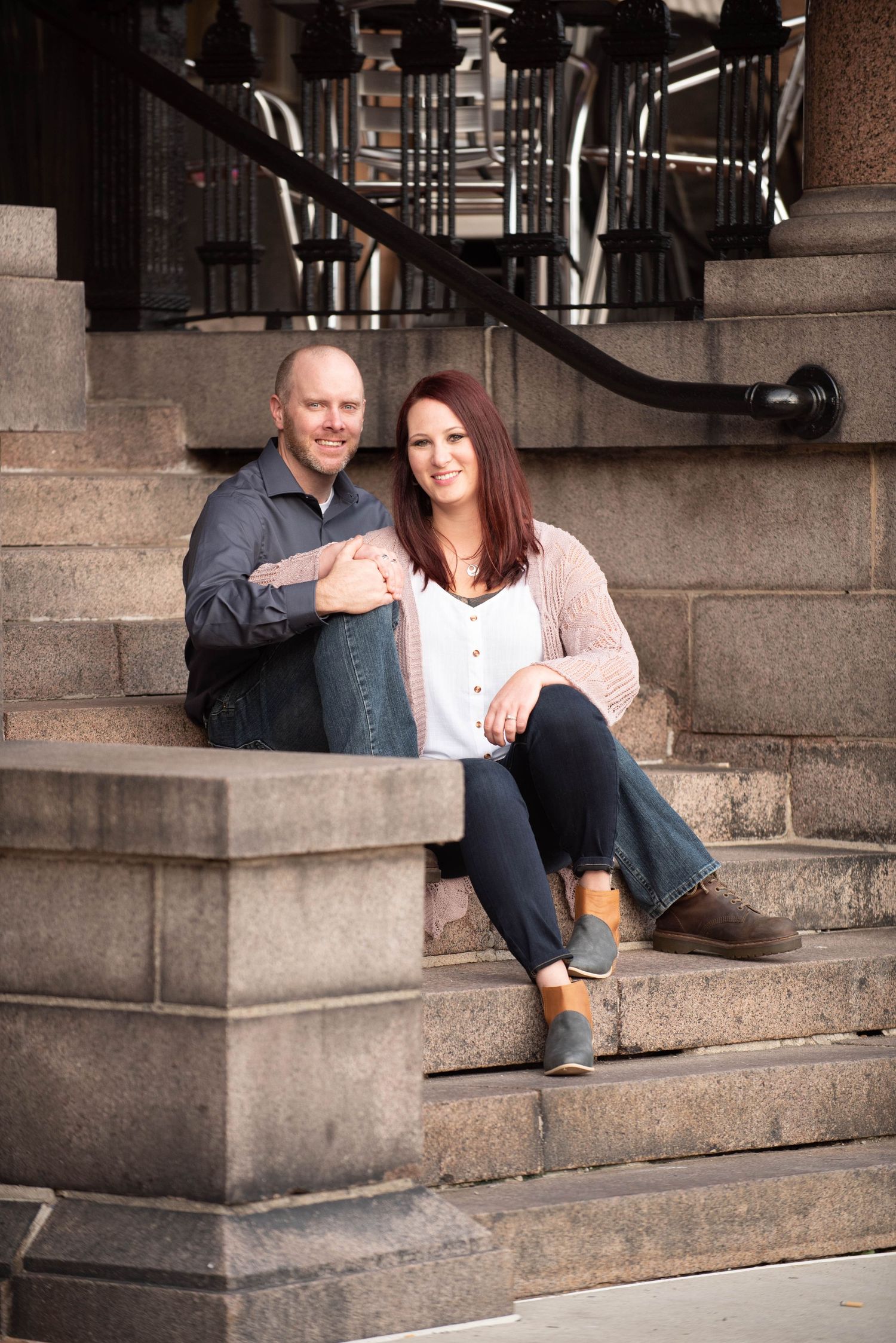 A couple relaxes on concrete steps outside a building with iron railings at sunset.