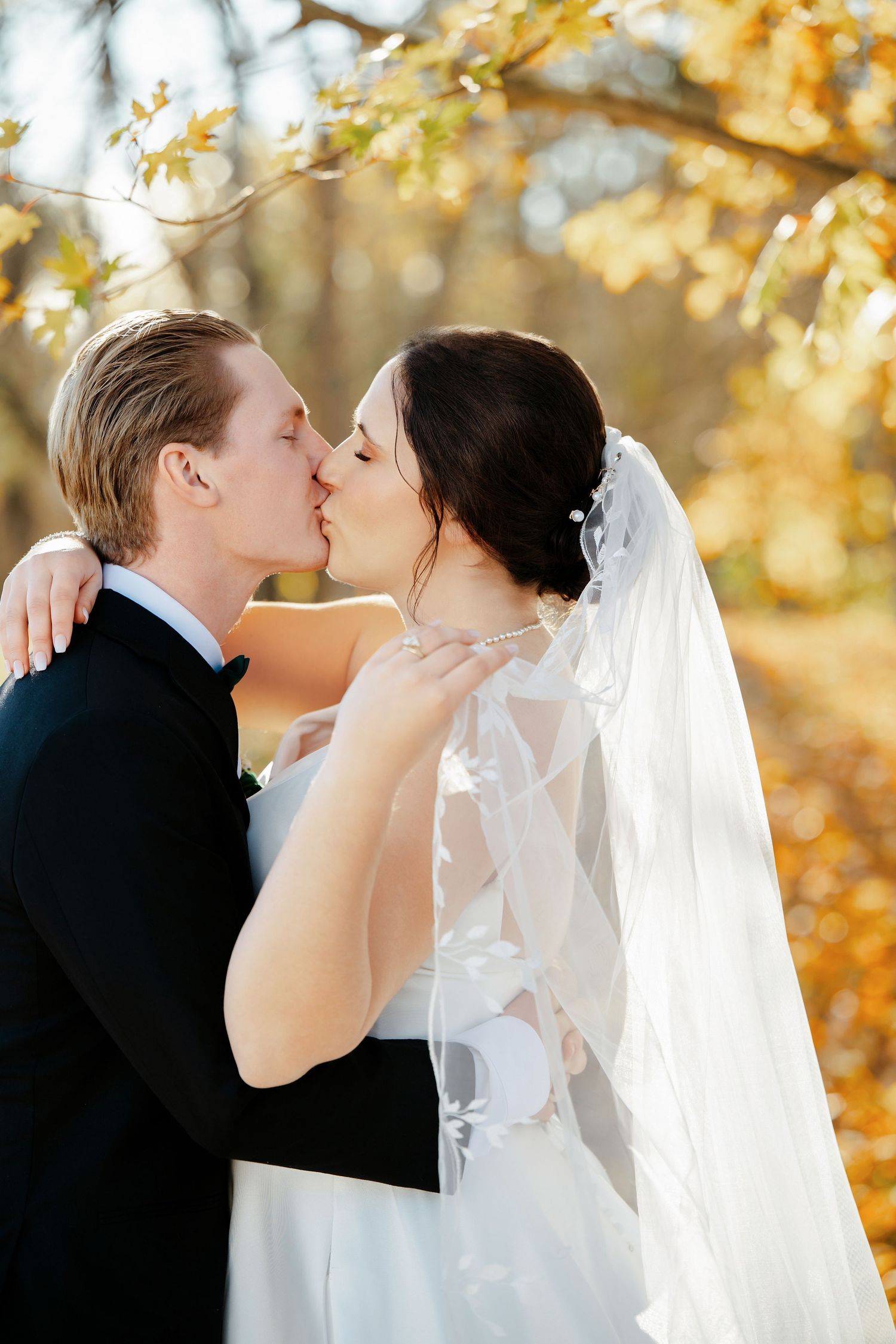 Tender wedding kiss captured in front of vibrant yellow fall foliage.