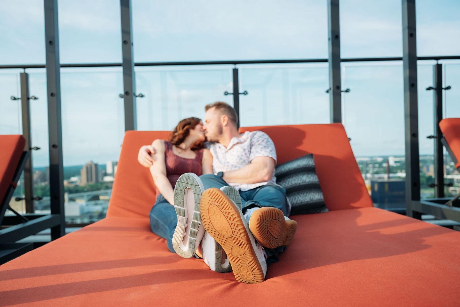 People relaxing on red lounge seating with city views through floor-to-ceiling windows.