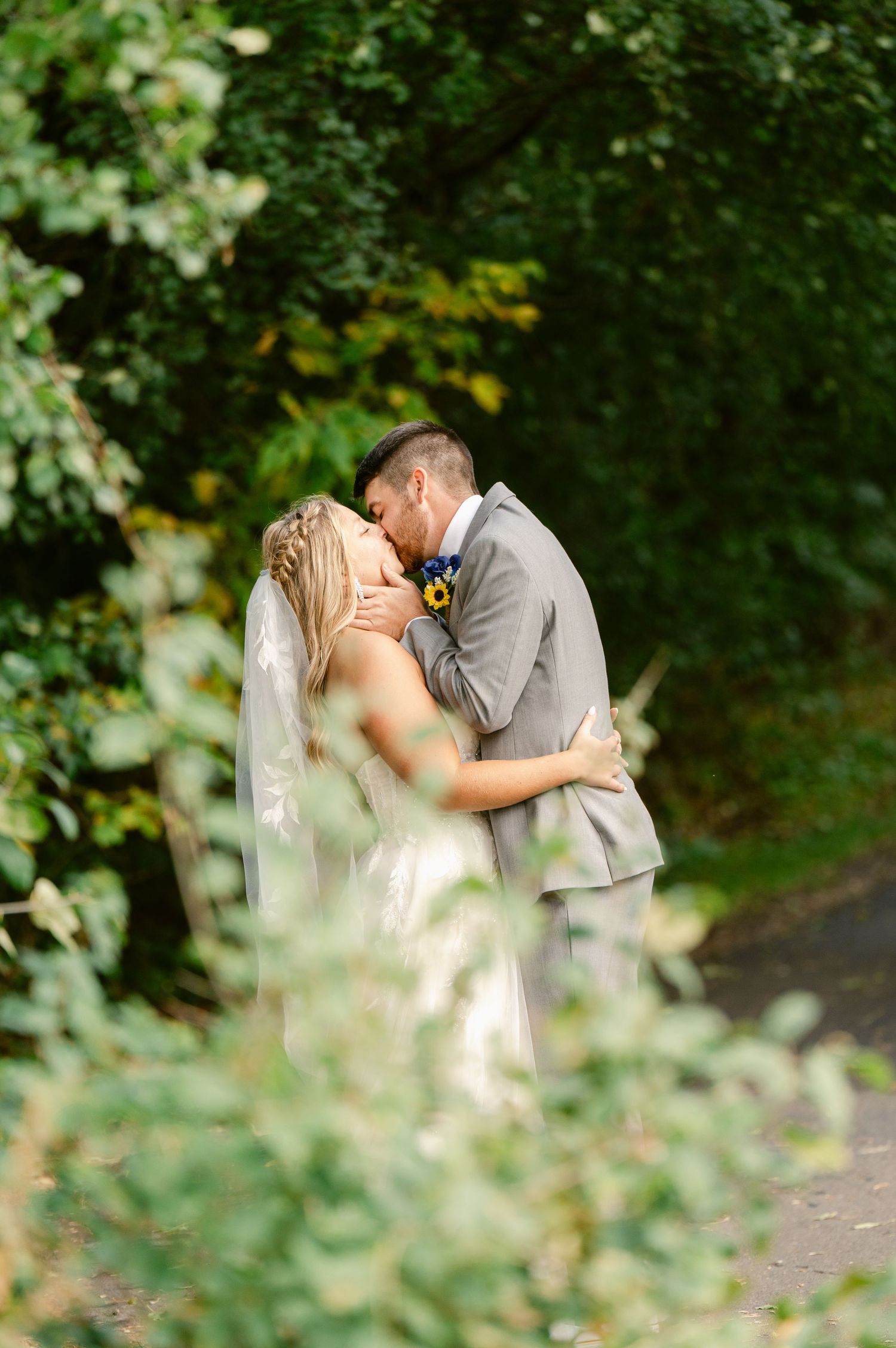 Central MN Wedding Photos | Bride and groom kissing surrounded by lush green foliage on wedding day.