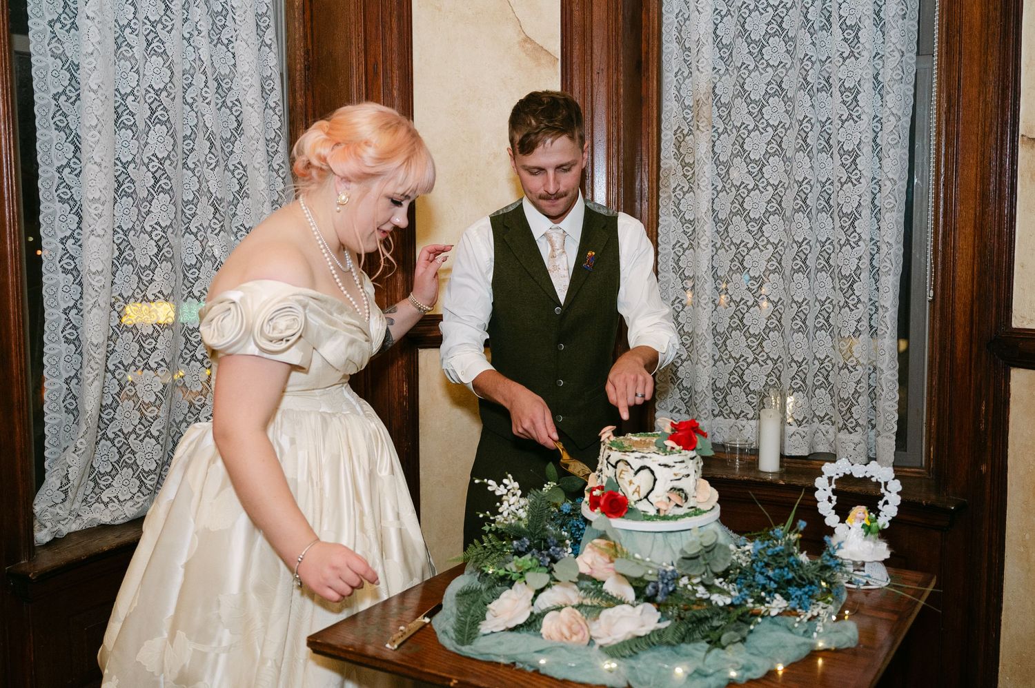 Central MN Wedding Photos | Bride and groom cutting their wedding cake decorated with greenery and flowers.