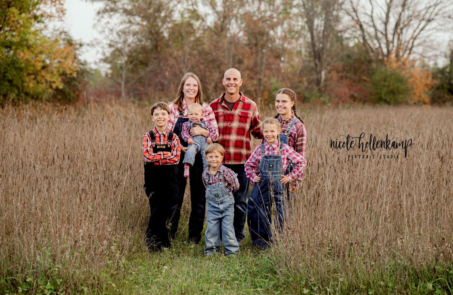 Family of five poses together in tall autumn grass wearing coordinating plaid shirts.