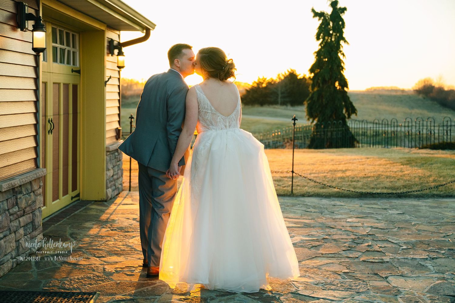 Bride and groom share a sunset kiss on a stone patio, golden light glowing behind them at an outdoor wedding venue. Crooked Willow Osakis