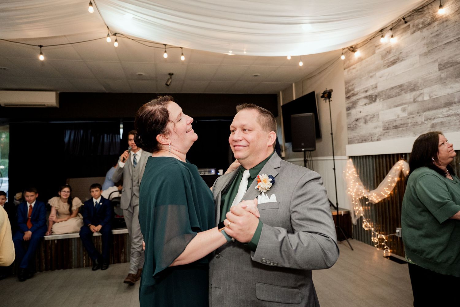 Panoramic view of wedding reception with white ceiling draping, string lights and couples dancing.
