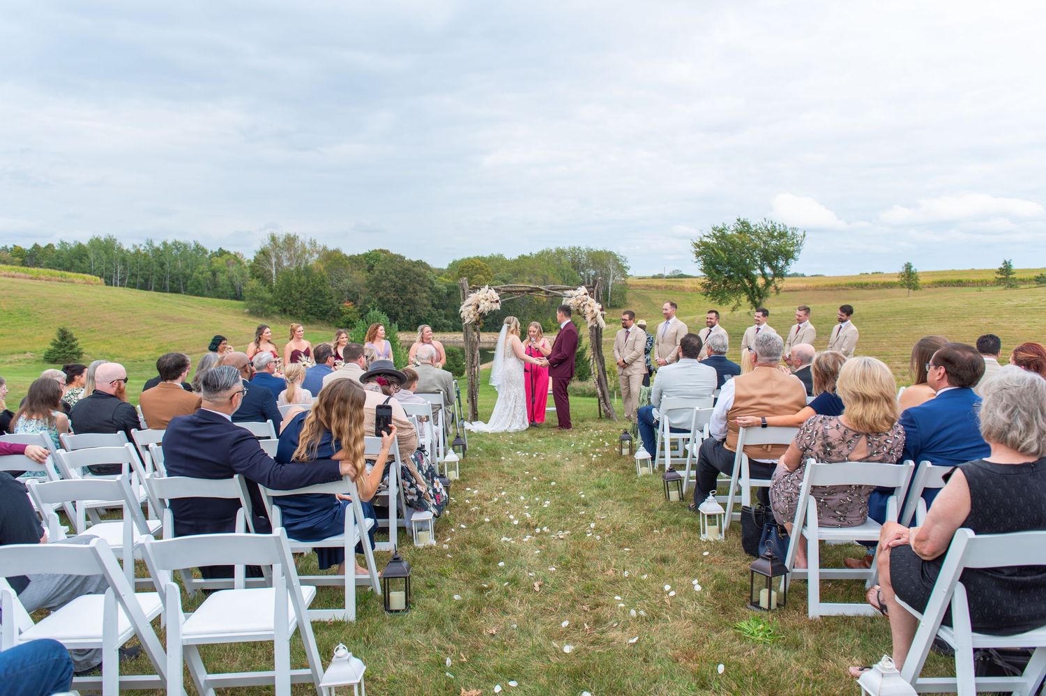 Guests seated in white chairs for outdoor wedding ceremony on rolling hillside.