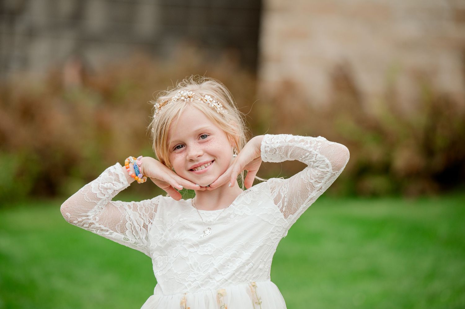 Young flower girl in lace dress plays playfully in garden setting.