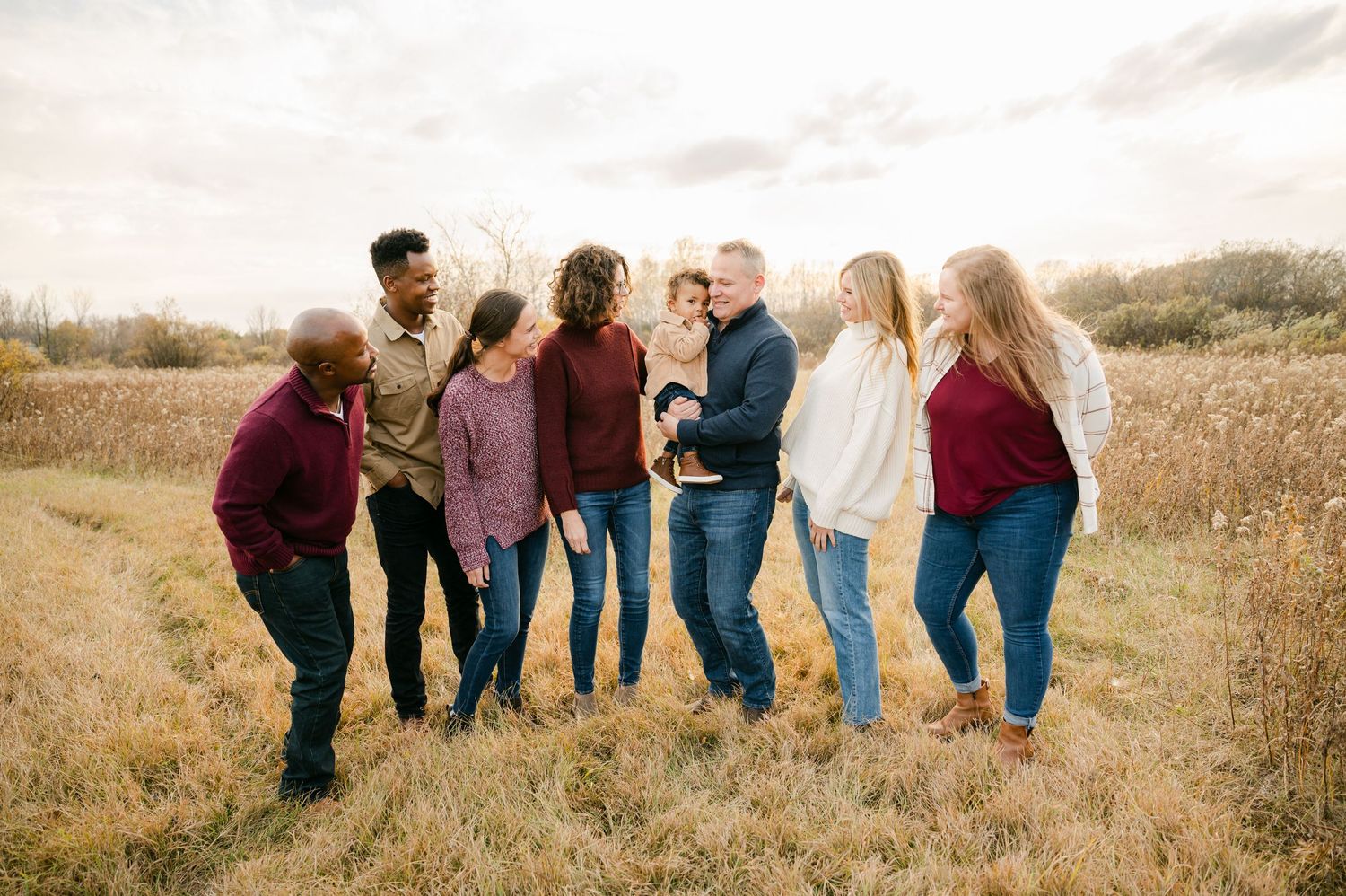 A group of friends laugh together while standing in a golden field during sunset.