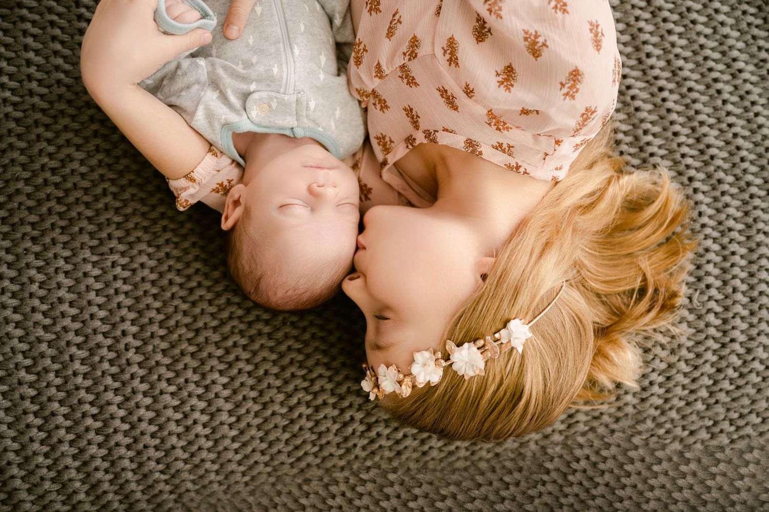 Sleeping baby wearing floral dress with bow lying on grey textured background in artistic composition.