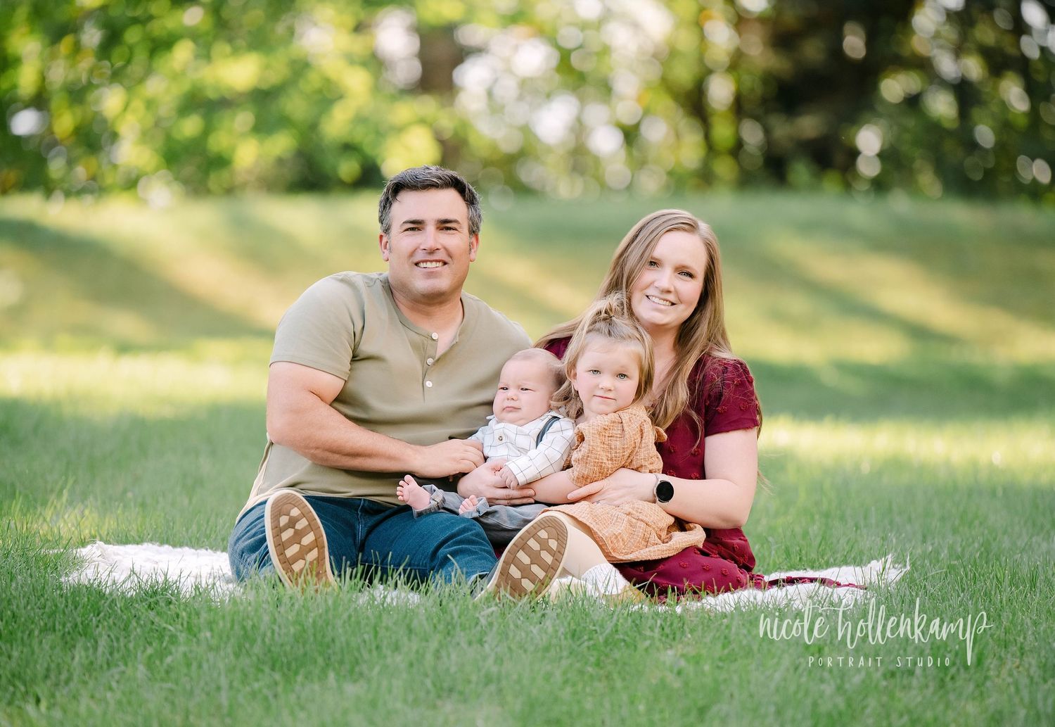 A couple lounges together on green grass during a sunny outdoor photo session in a park setting.