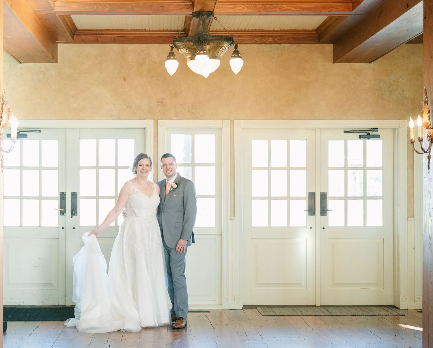 Bride and groom posing together in front of elegant French doors in a warmly lit historic venue.