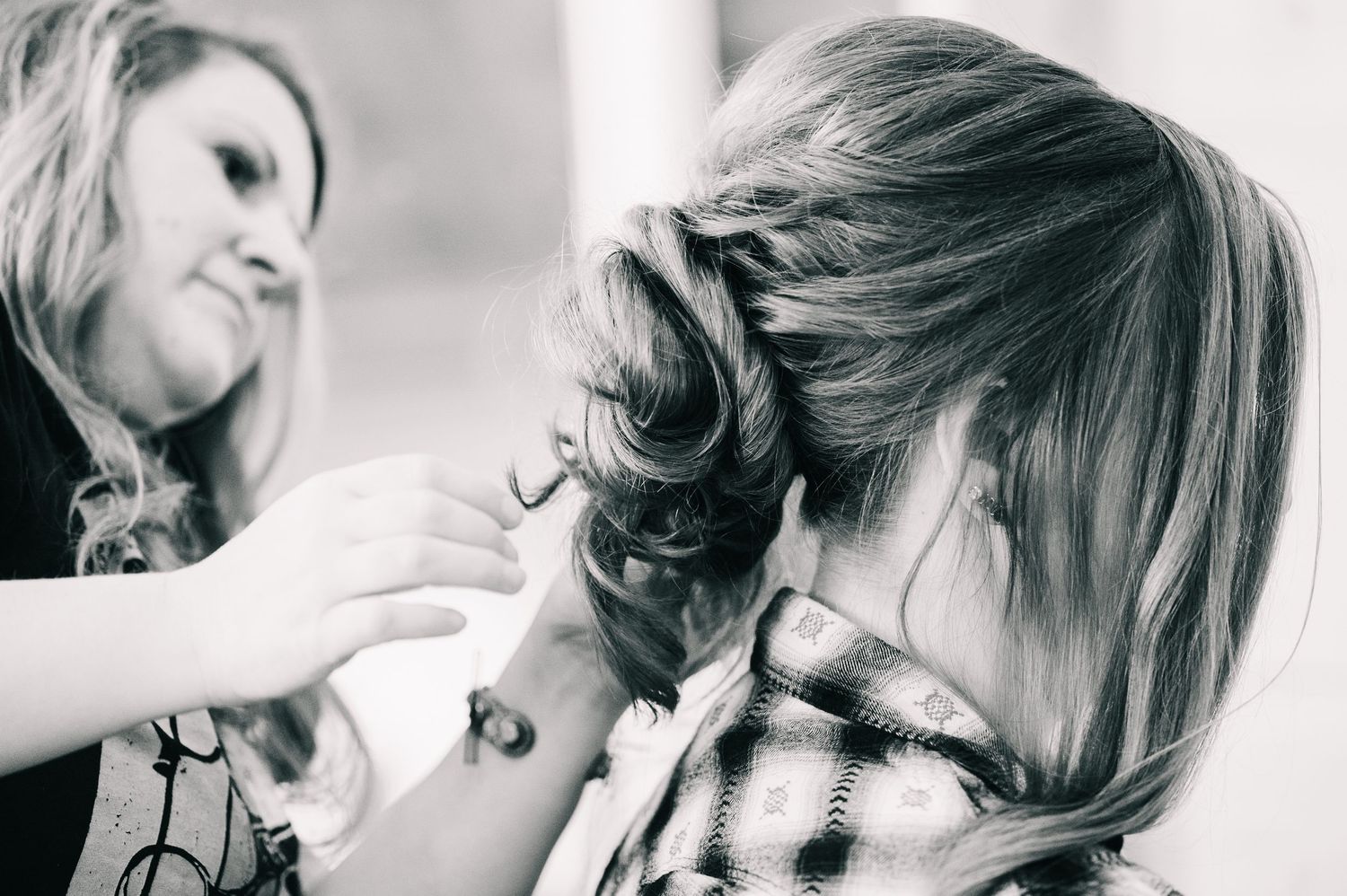 Black and white photo of a hairstylist pinning up an elegant braided updo on a woman at a wedding.