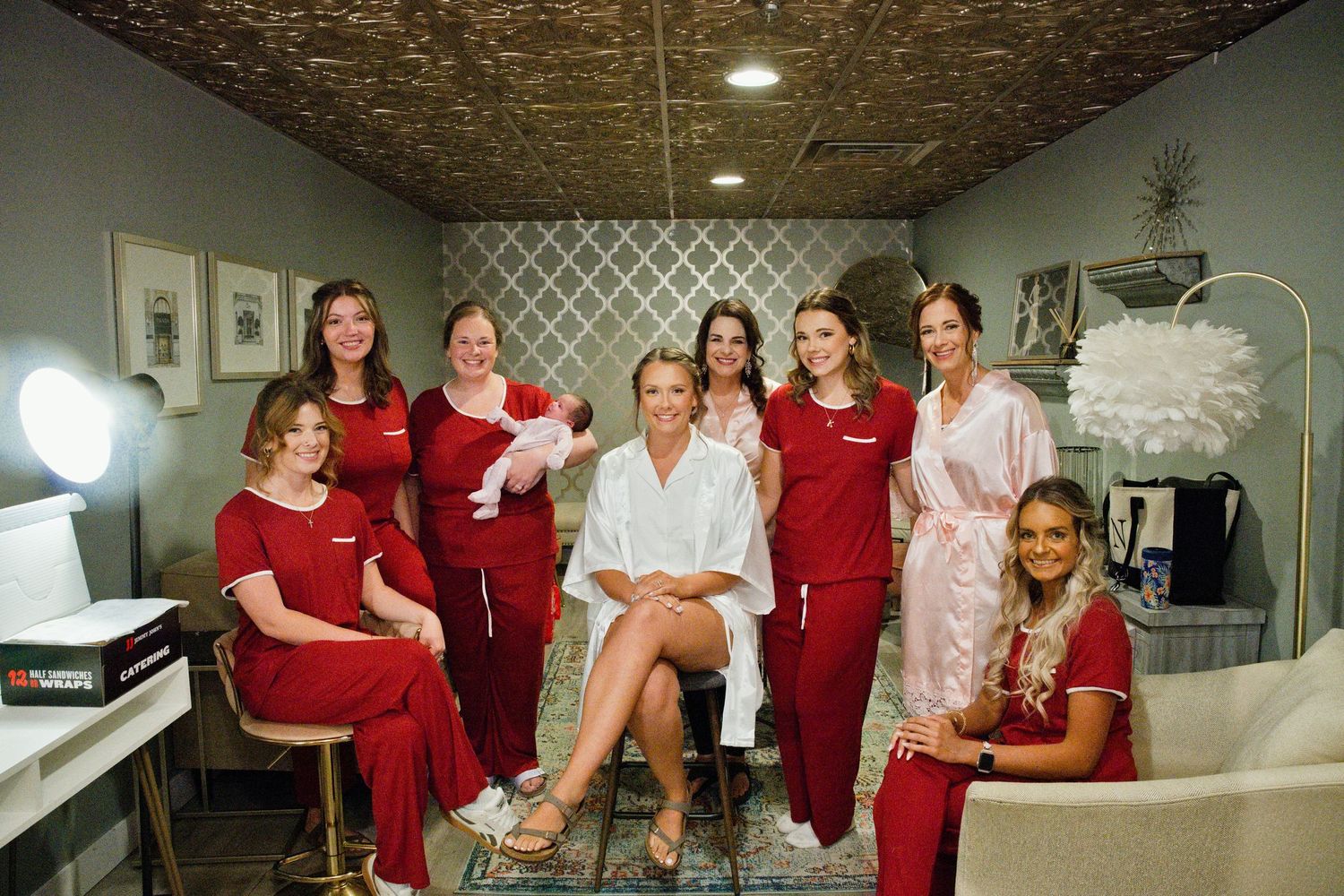 Bride in white robe surrounded by bridesmaids in red at a bridal getting-ready suite.