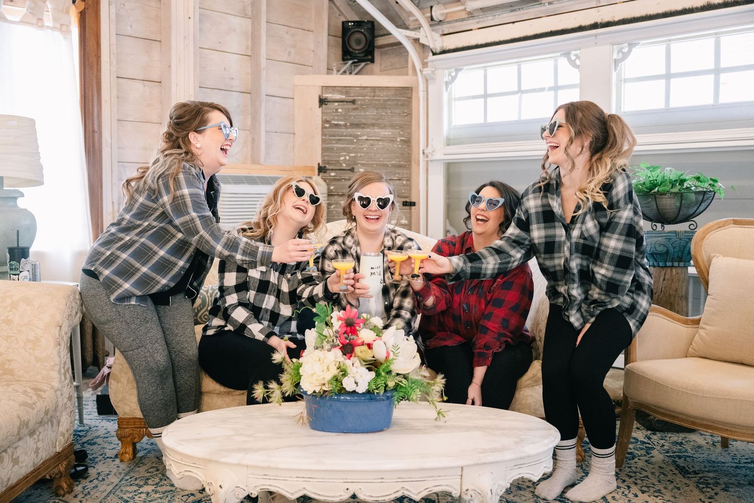 crooked willow weddings Five women in matching plaid shirts celebrating together in a rustic venue setting.