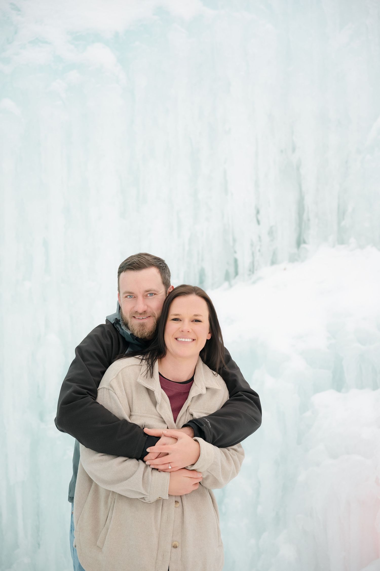 Couple embracing and smiling in front of a stunning ice castle wall backdrop in winter. Engagement Minneapolis MN