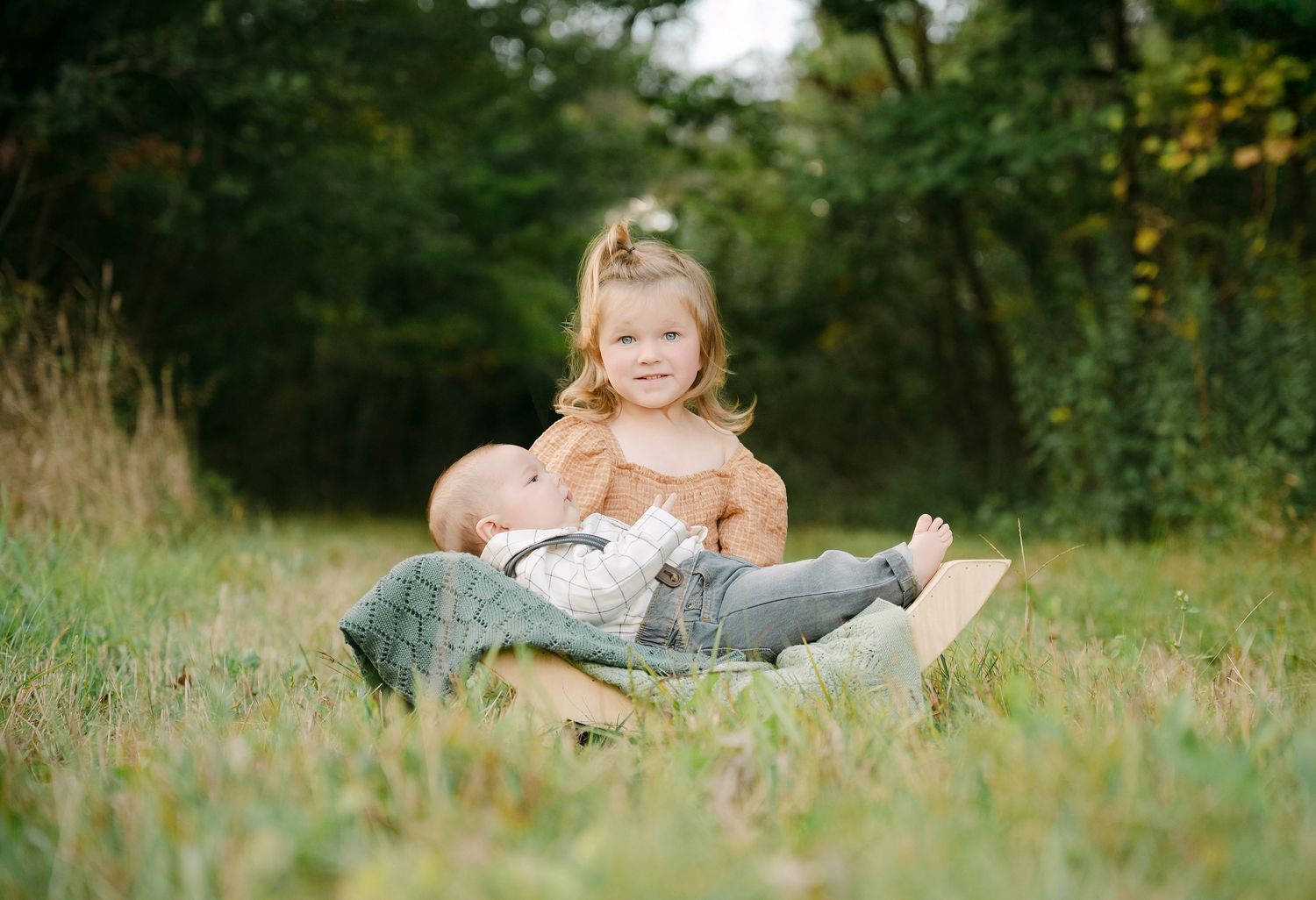 Young girl sitting outdoors in grass holding a teddy bear during a family photo session.. Minnesota milestone photographer