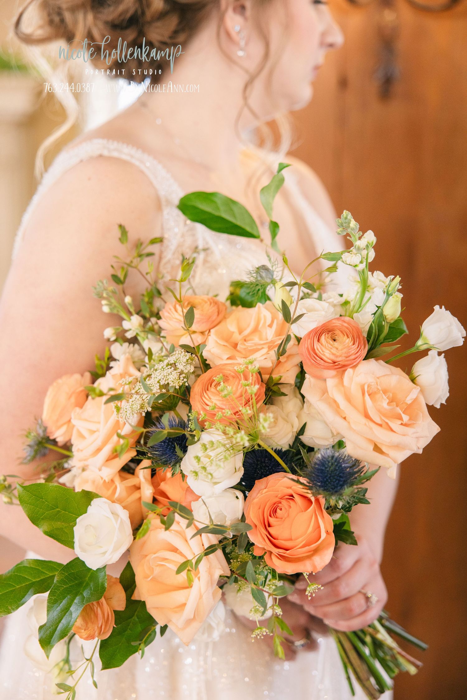 Bride holding a lush peach and white wedding bouquet with roses, ranunculus, and blue thistle accents. Crooked Willow Osakis