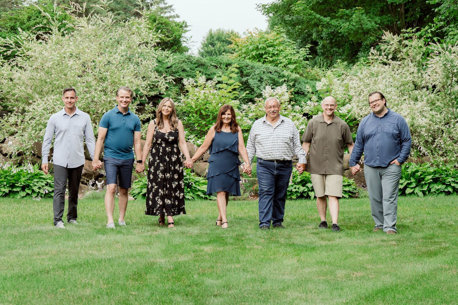 Small group standing casually on manicured lawn with blooming bushes in background.