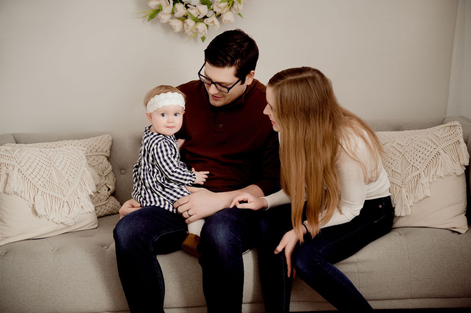 Young family sits together on white couch in minimalist indoor setting.
