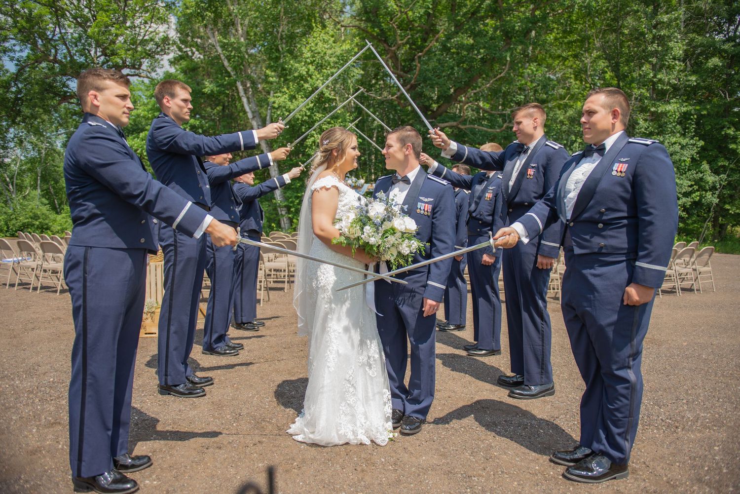 Wedding party in navy uniforms and formal attire forms an archway with swords for a couple during an outdoor ceremony. Zimmerman MN Weddings