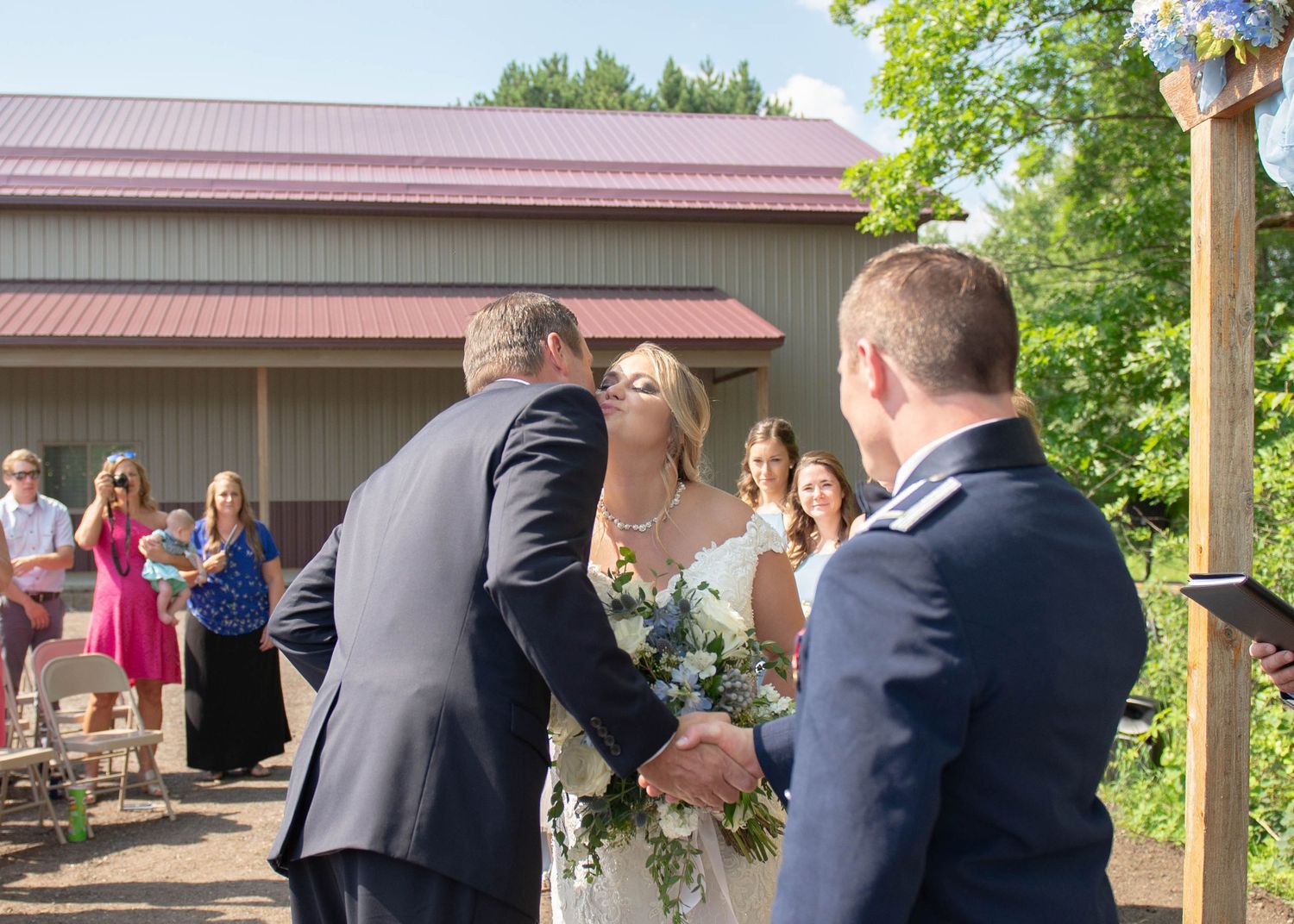 Wedding couple exchanging vows during outdoor ceremony under wooden arbor. Zimmerman MN Weddings