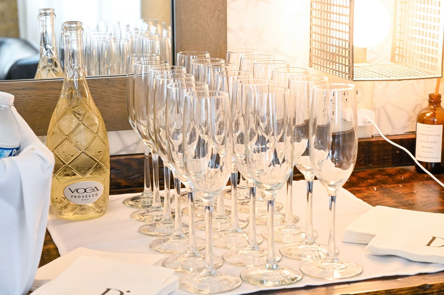 Multiple rows of empty wine glasses and champagne flutes arranged on white tablecloths at an elegant event setting.