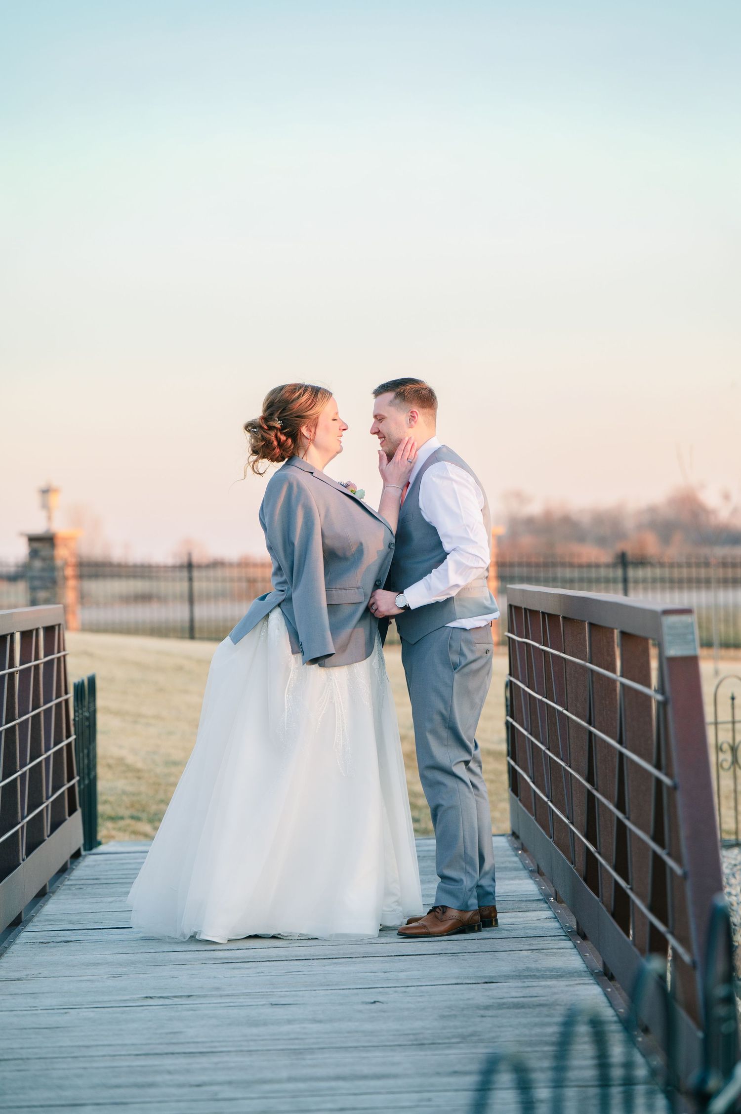 Bride and groom share a romantic moment on a wooden bridge at sunset during their wedding.