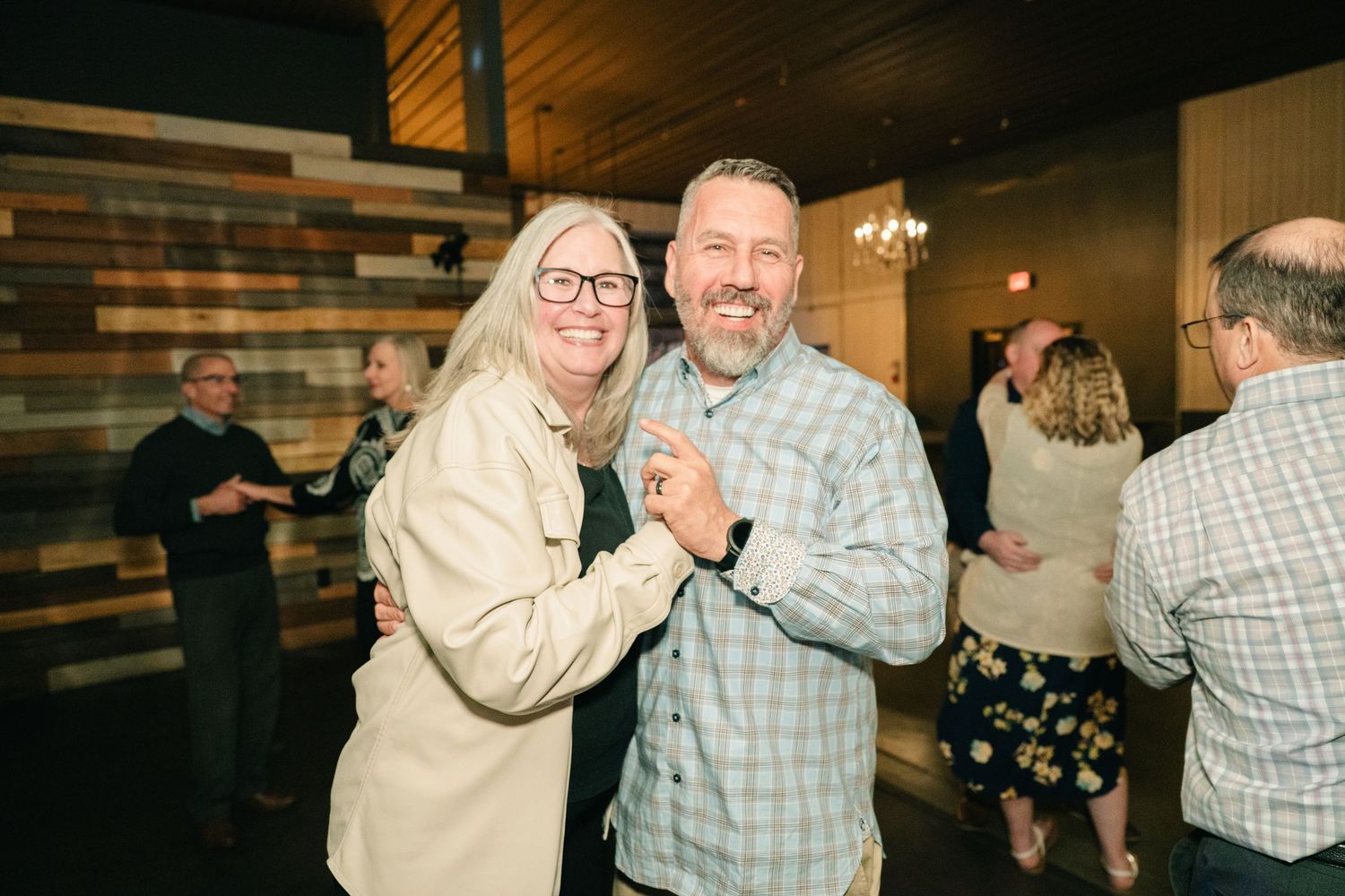 Couple dances and smiles together at a lively wedding reception in a rustic venue.