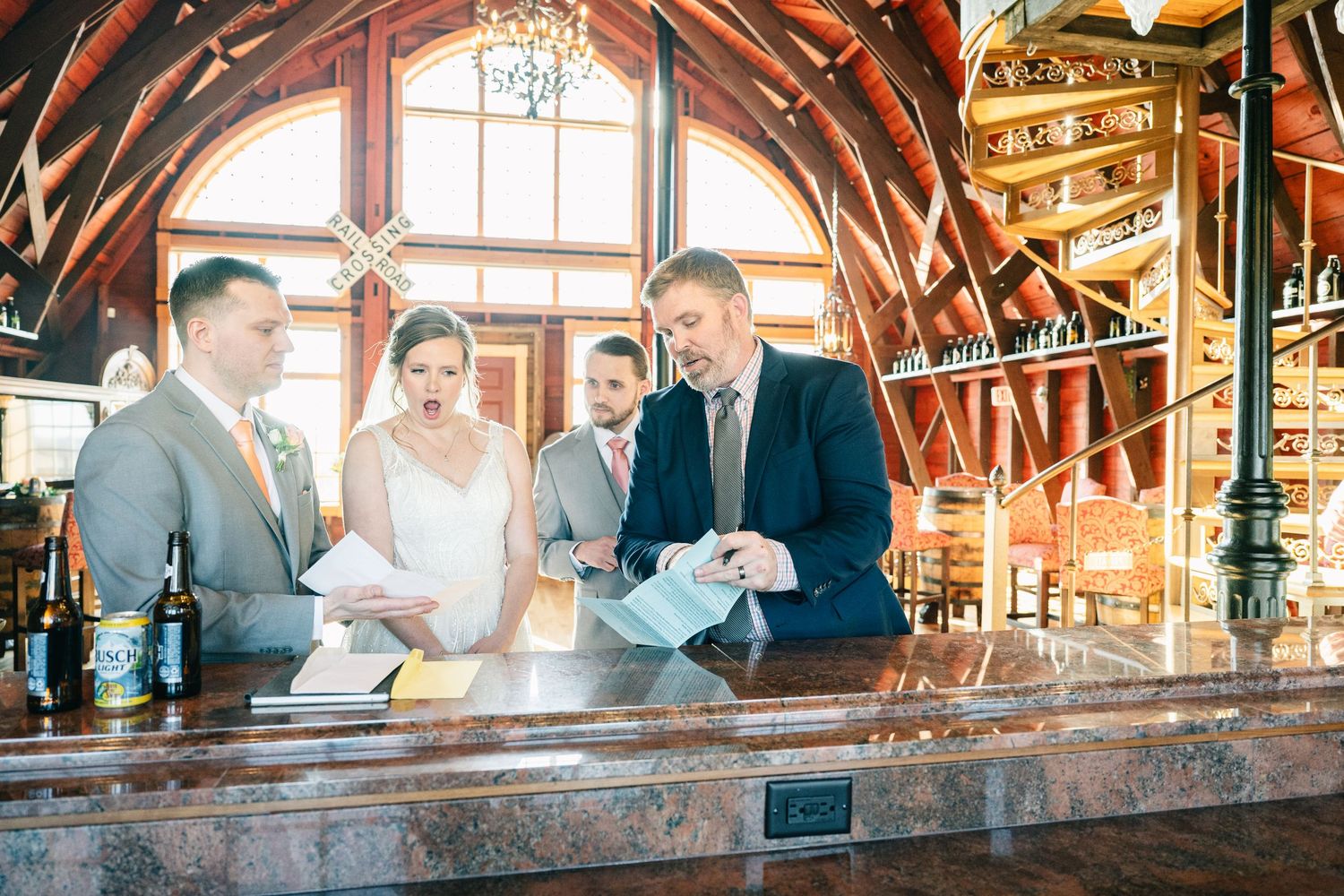 Bride and groom signing wedding documents at ornate wooden bar with wine bottle display.