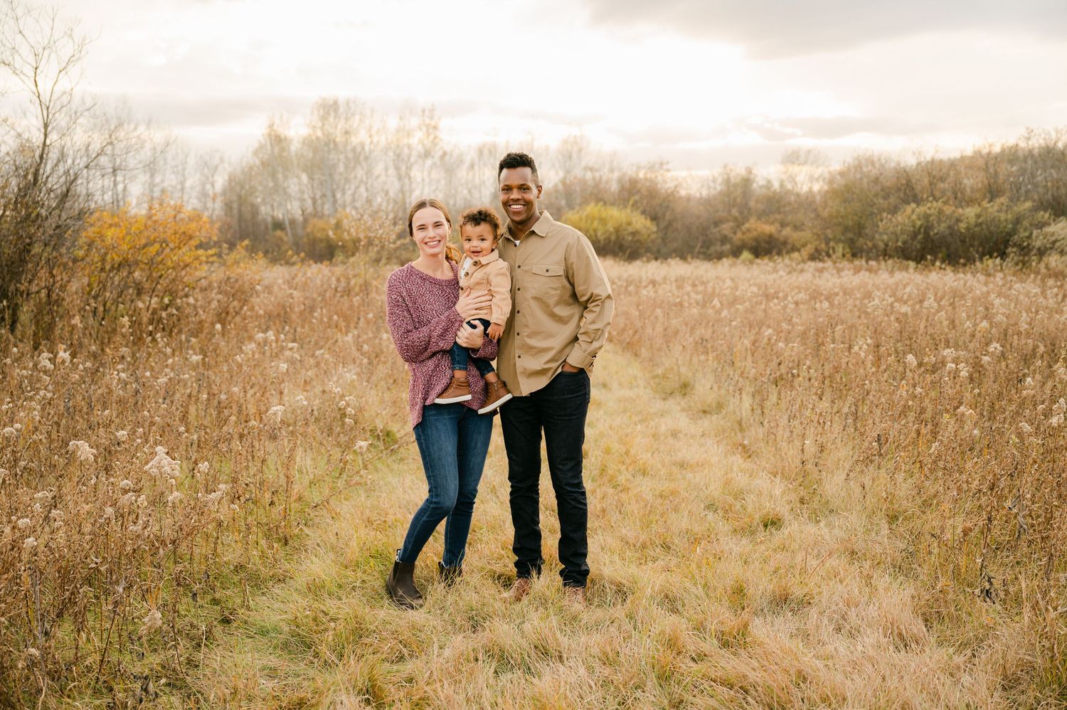 A couple embraces in a golden autumn field during sunset with tall grass and warm tones all around them.
