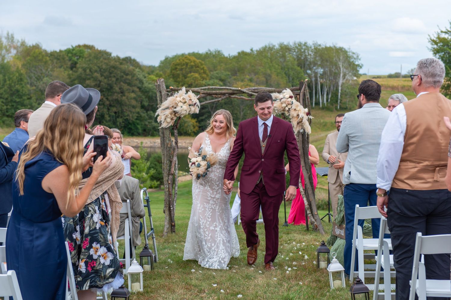 Wedding party walks down aisle while guests celebrate at outdoor ceremony.