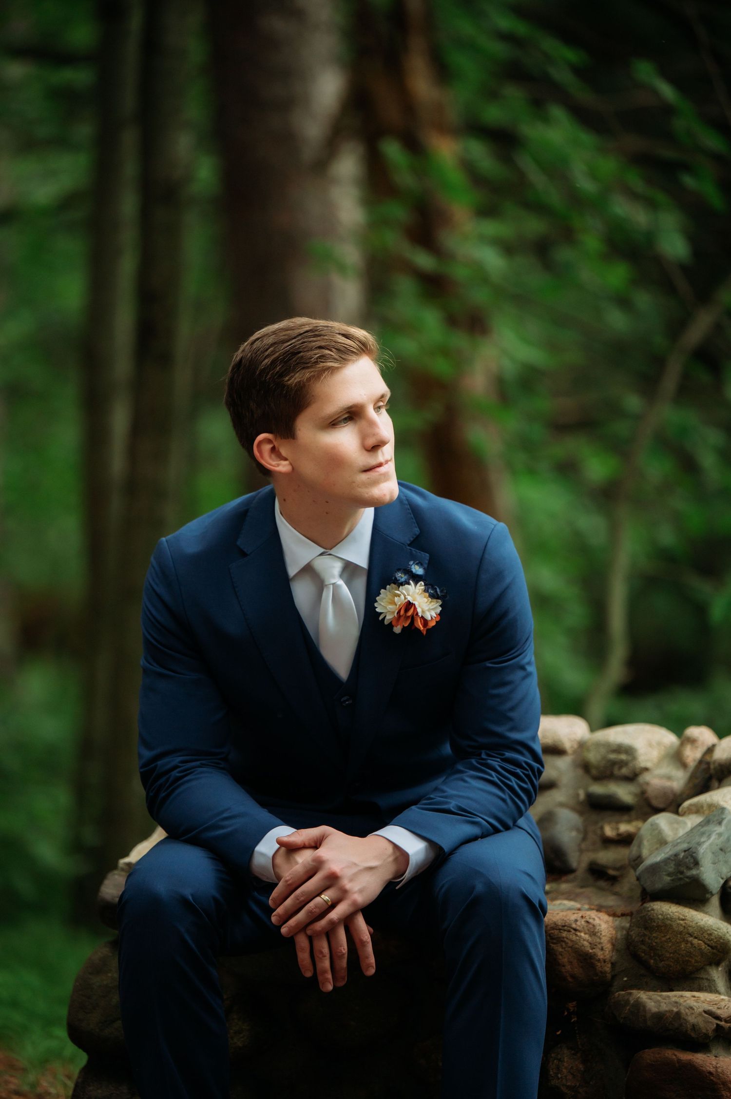 A formal portrait in a navy suit against a moody forest backdrop.
