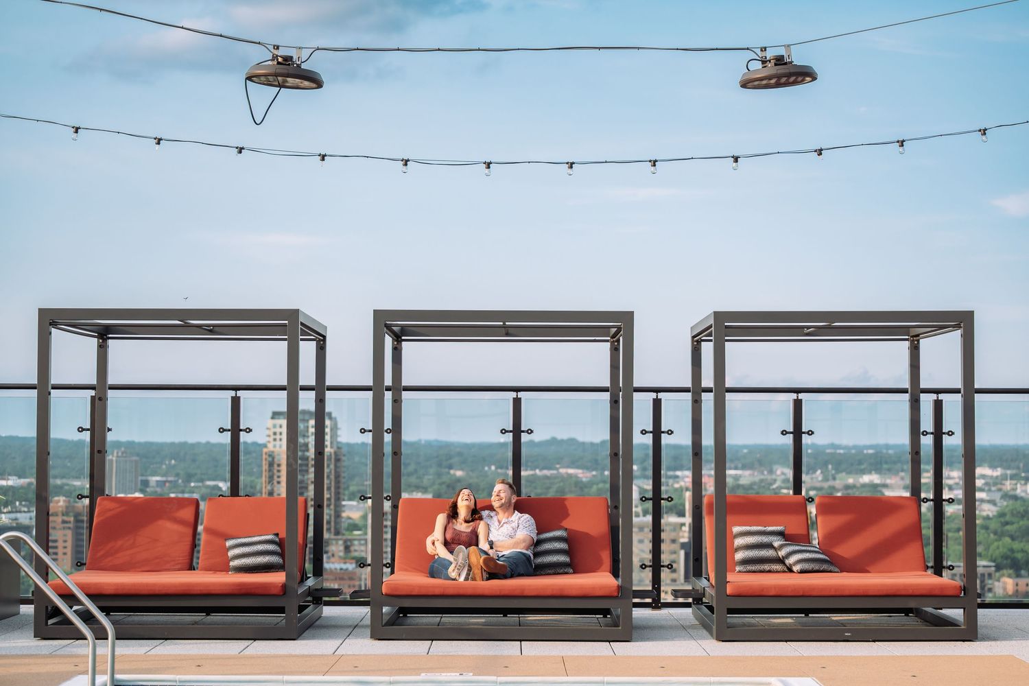 Modern outdoor lounge area with orange cushioned seating and string lights overlooking a city view.