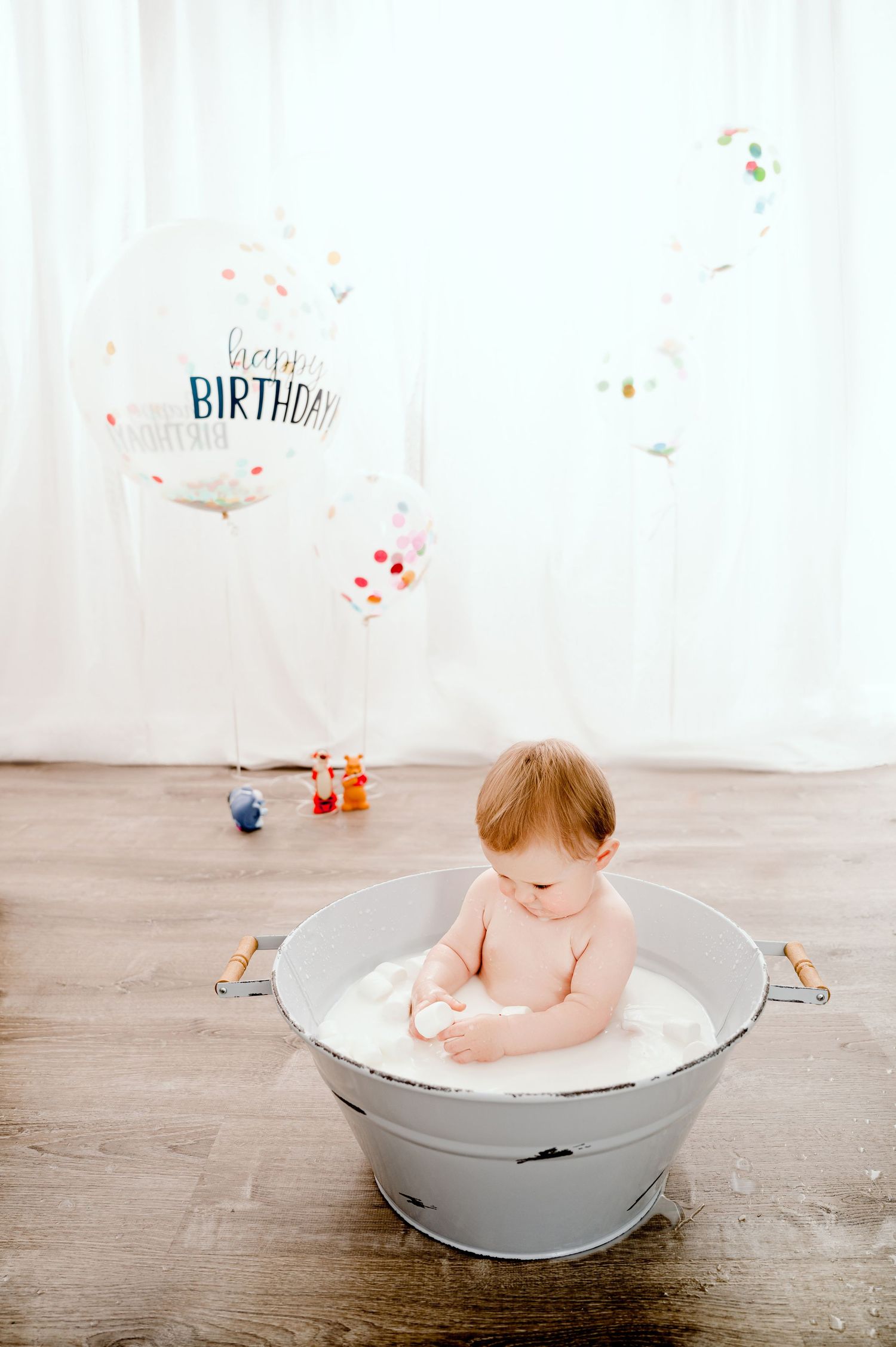 Central MN smash Photography - Baby sitting in a galvanized tub with milk during a first birthday cake smash photoshoot with balloons.