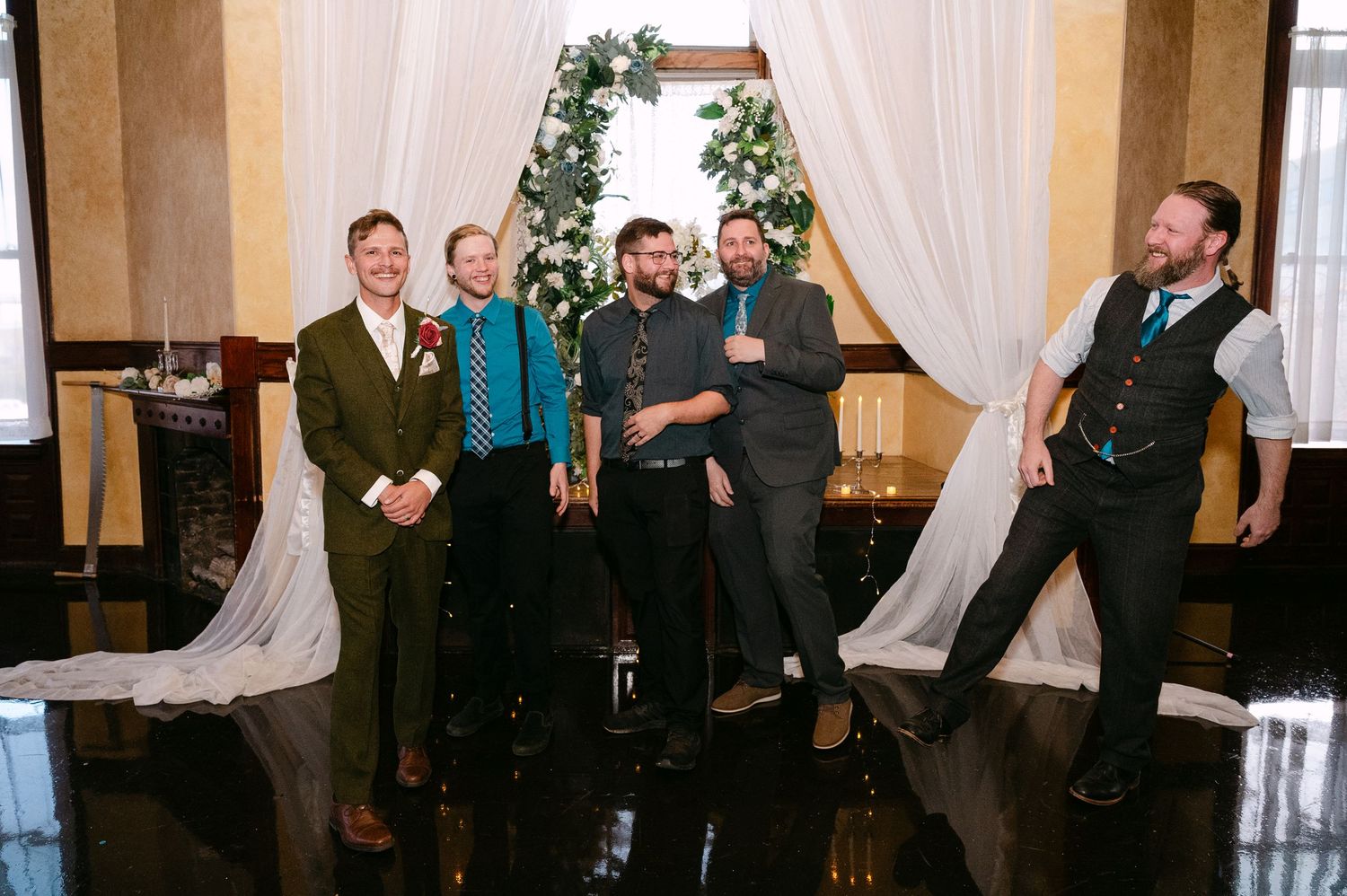 Central MN Wedding Photos | Wedding party group laughing and celebrating near greenery arch backdrop at elegant venue reception.