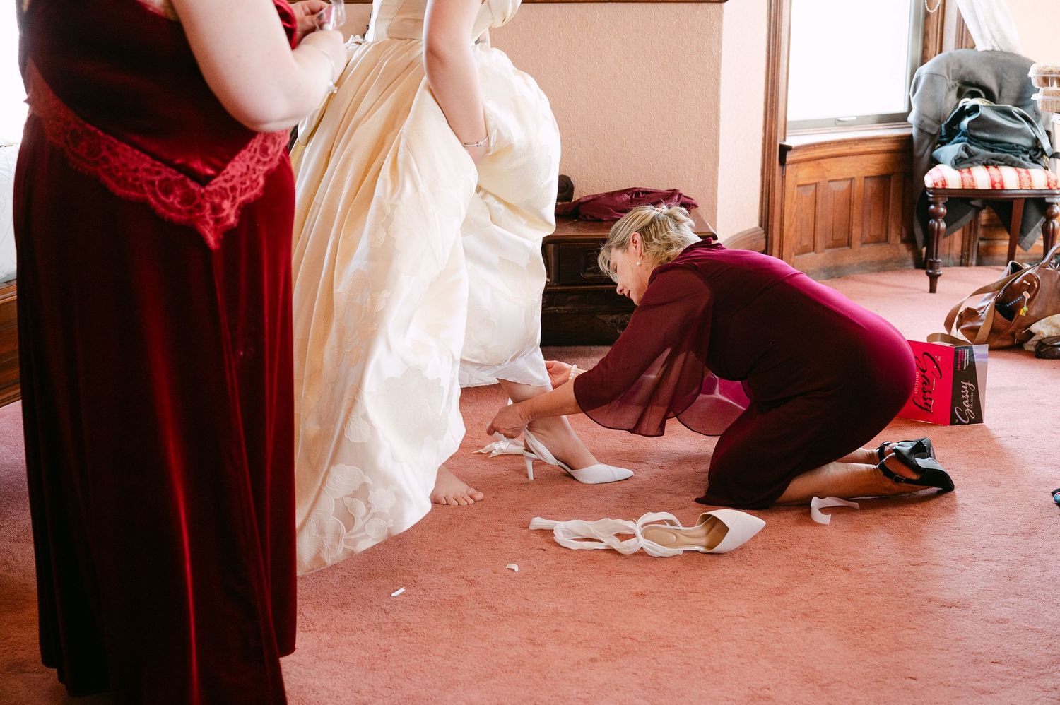 Central MN Wedding Photos | Bridesmaid kneeling to help bride with her wedding shoes while another bridesmaid stands nearby.