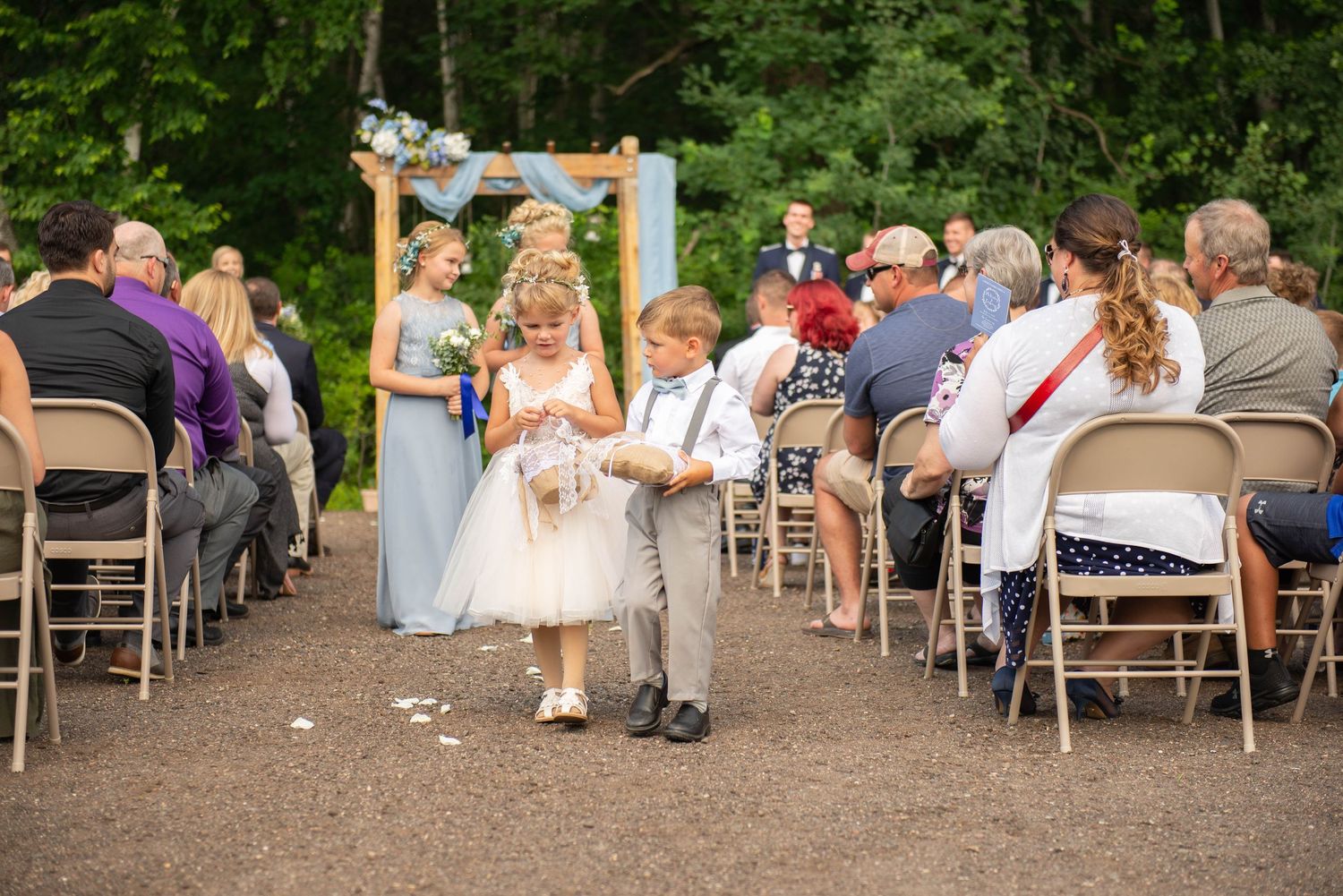 Young flower girl and ring bearer walk down aisle at outdoor wedding ceremony. Zimmerman MN Weddings