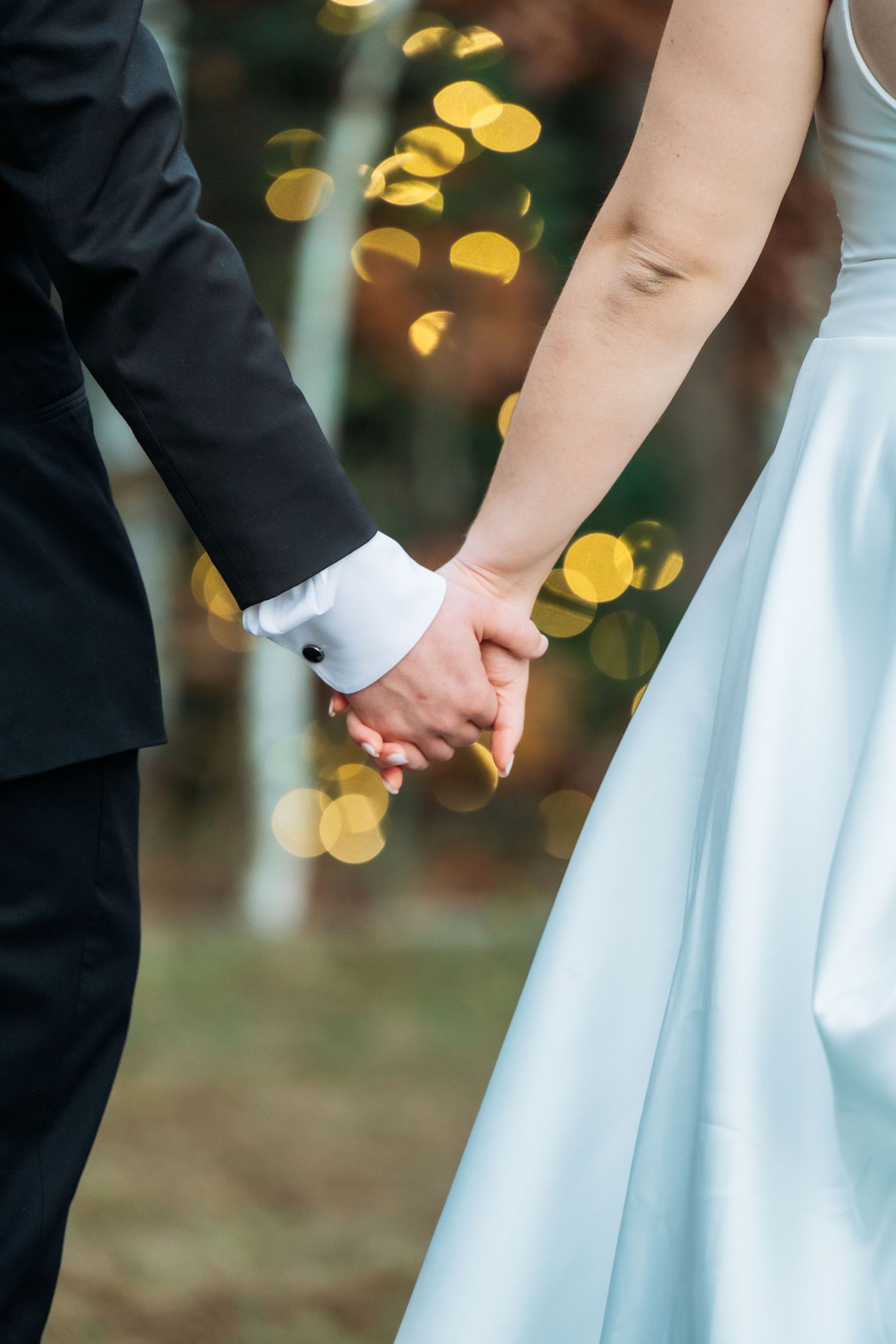 Close-up of newlyweds holding hands with bride in white dress and groom in black suit.