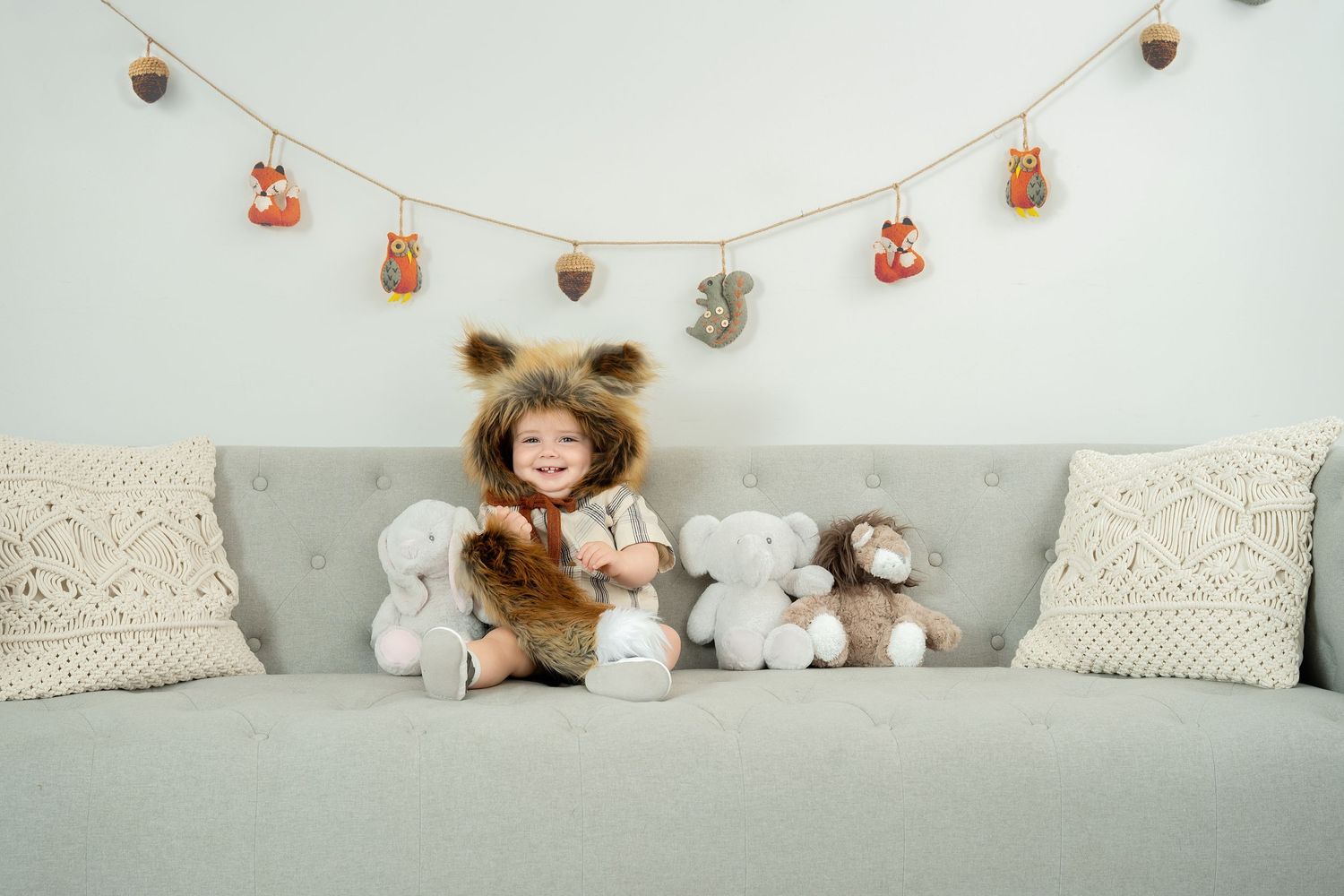 A cozy gray couch decorated with plush toys and a string of festive decorations hanging above.