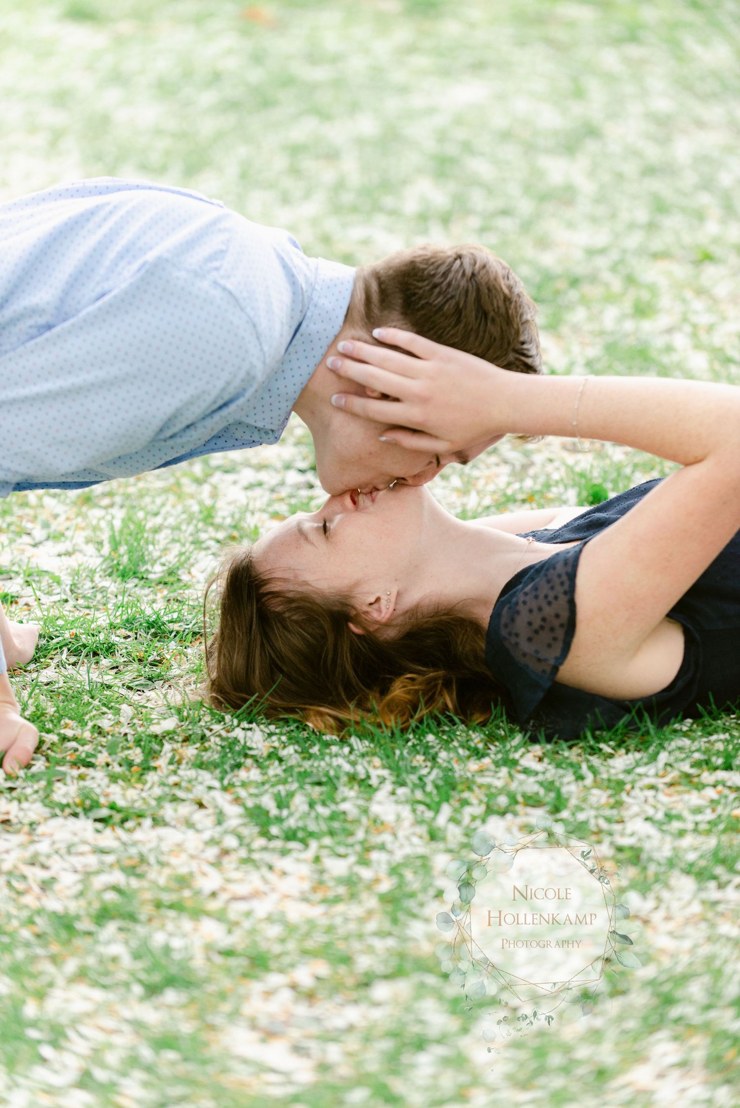 Couple shares a tender embrace while lying together on grass in a romantic outdoor engagement photo.