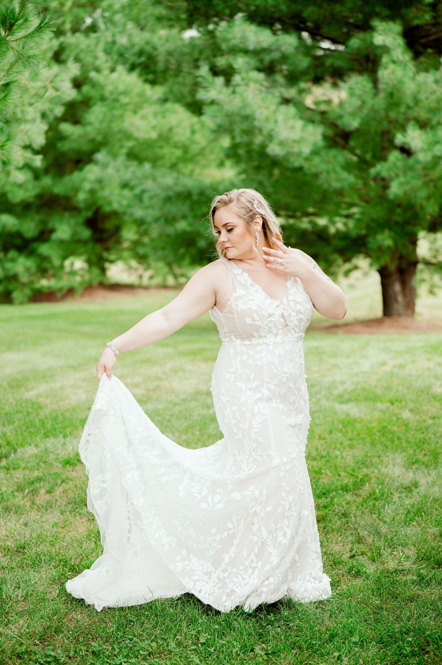 Bride in lace wedding dress twirls gracefully on a grassy lawn.