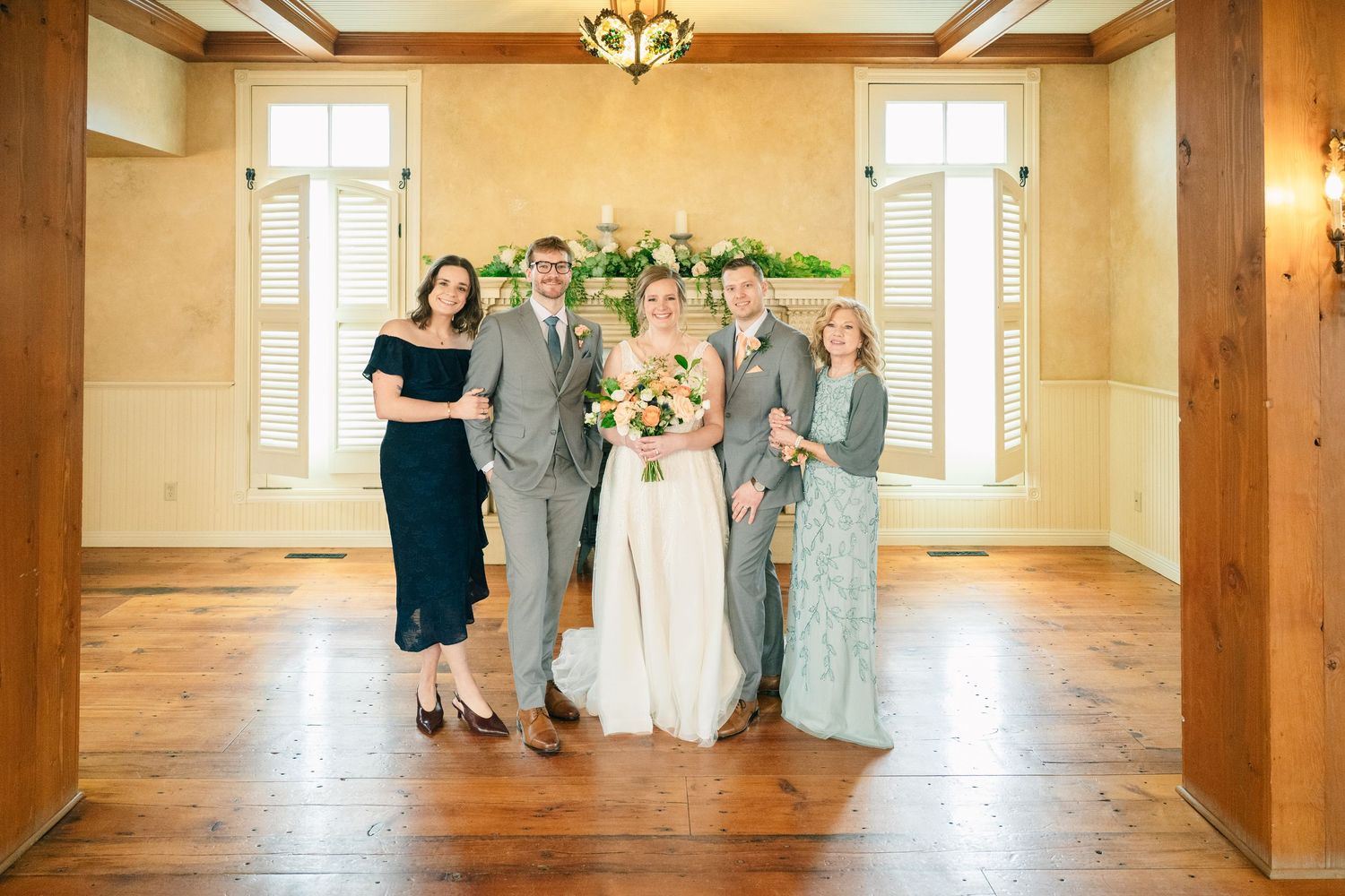 Wedding party family portrait with bride in white gown and guests in formal attire indoors.